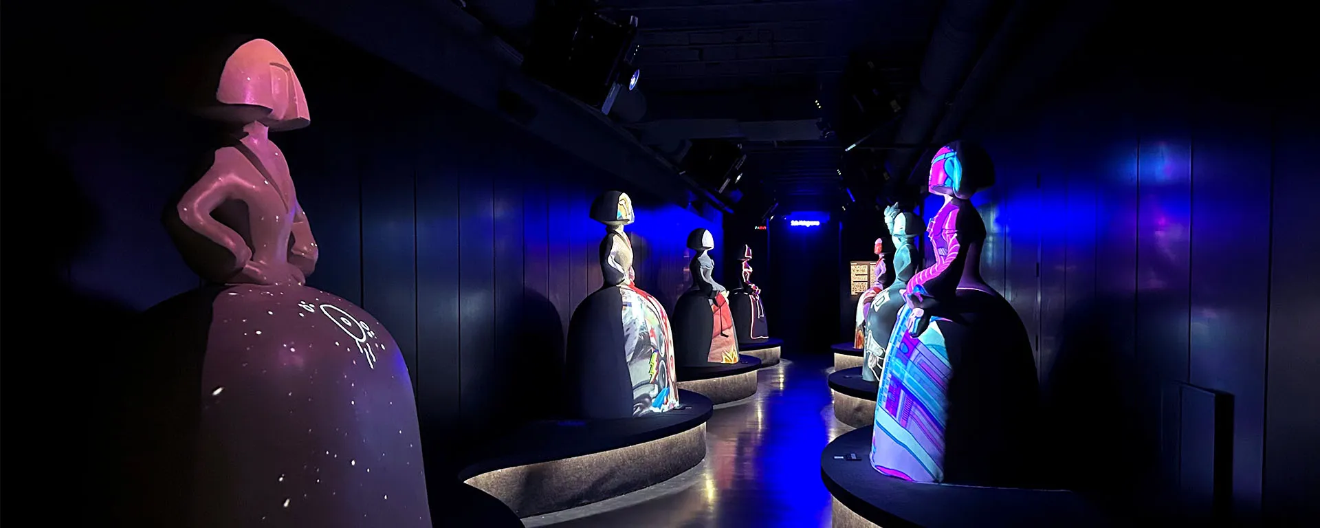 Dark gallery with illuminated sculptures of figures from Las Meninas under blue and purple lighting