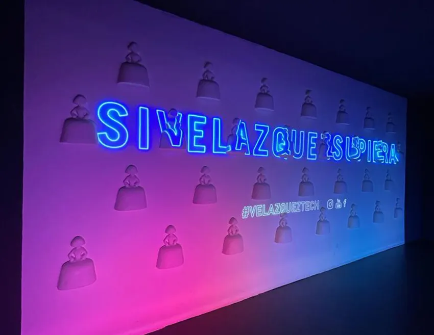 Neon sign reading 'SIVELAZQUEZ'UPERA' with sculptural figures on a purple and pink gradient wall
