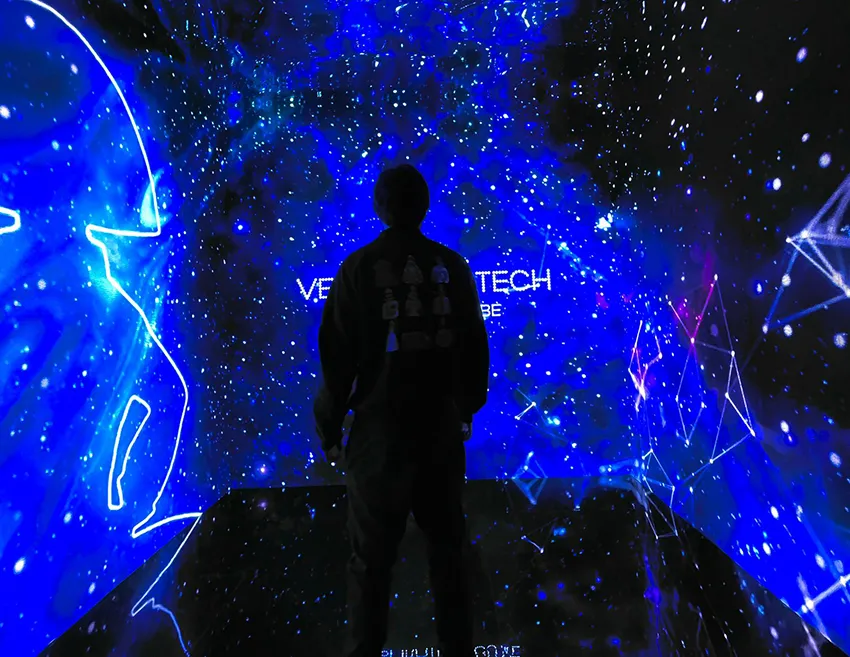 Silhouette of a person standing in front of a blue light projection with geometric patterns and the text 'VELAZQUEZ TECH' on the wall