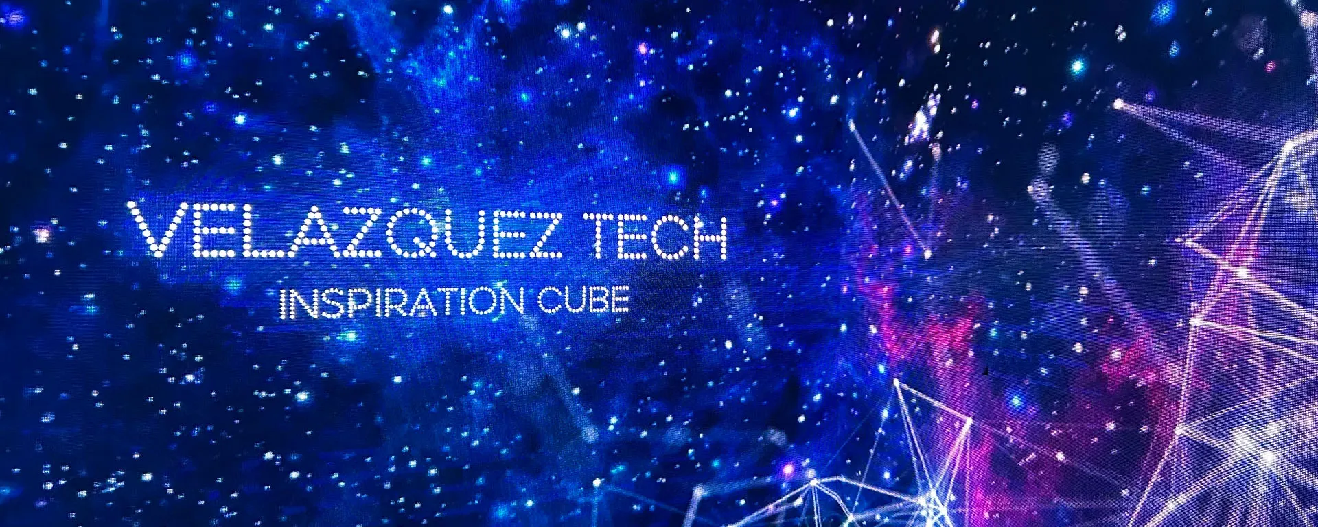 Velázquez Tech Inspiration Cube logo on a starry blue and purple background with geometric light lines