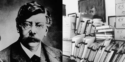 Retrato en blanco y negro de un hombre con gafas y bigote junto a pilas de documentos de archivo y libros
