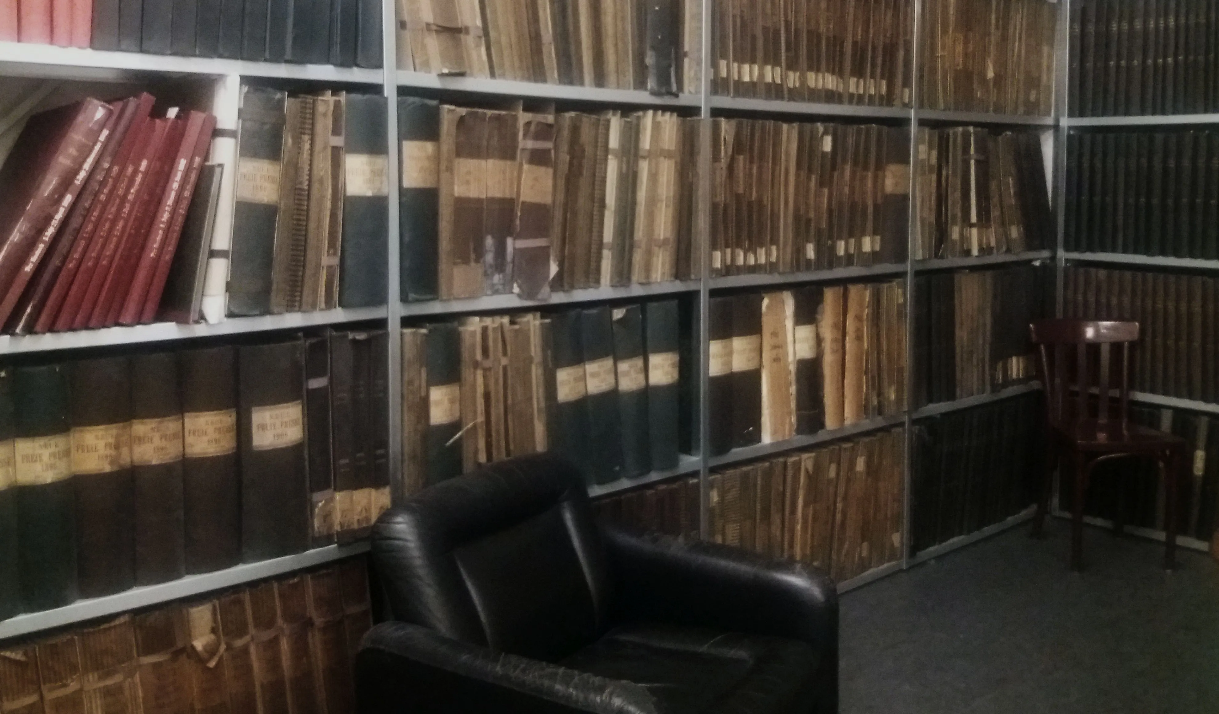 filas de libros y documentos antiguos en estanterías metálicas en una sala de biblioteca con una silla de cuero negro