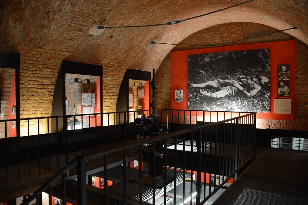 Interior de un museo con techos abovedados de ladrillo, una barandilla de escalera de metal negro y una gran fotografía en blanco y negro sobre una pared roja.