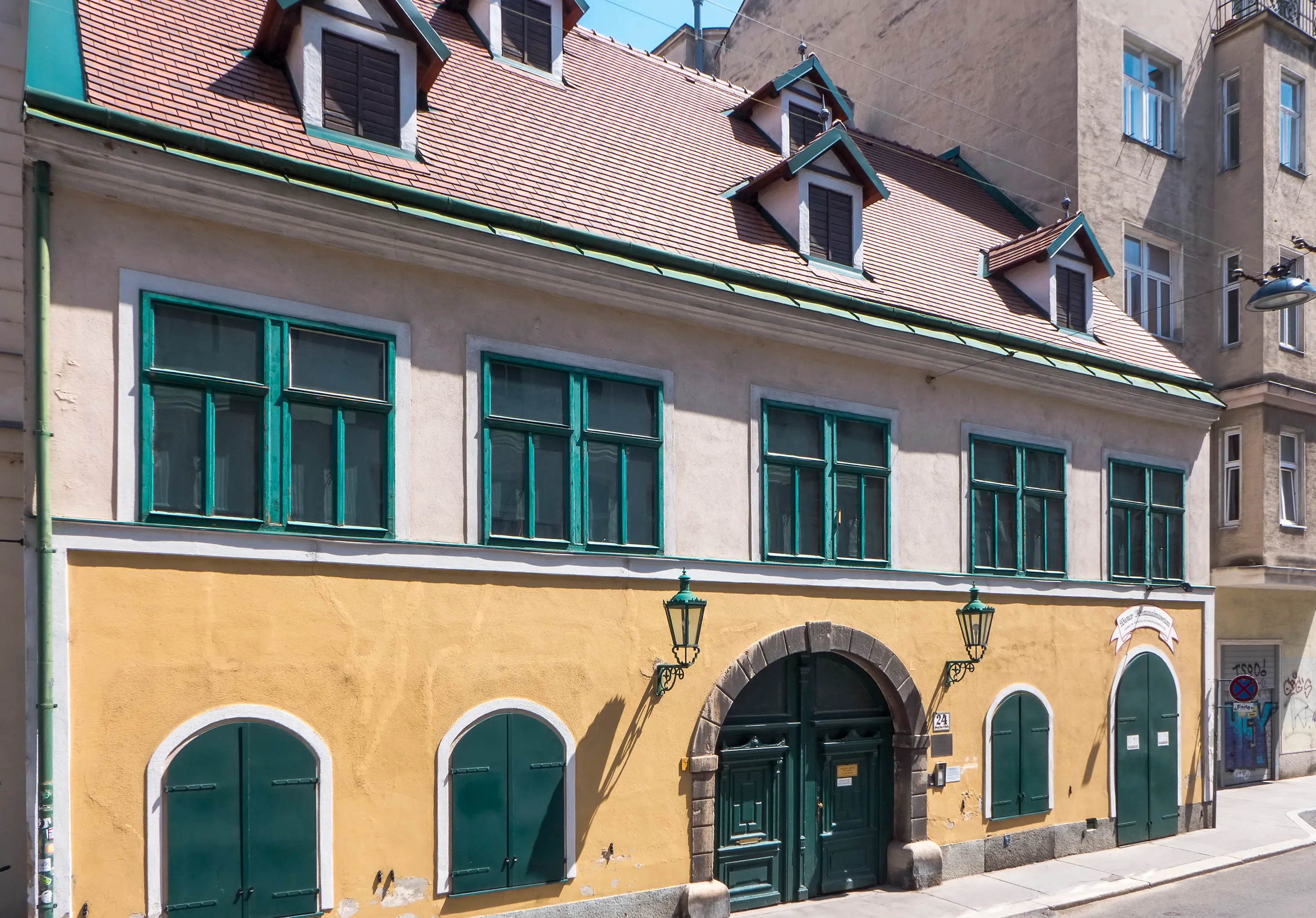 Edificio amarillo con ventanas verdes y puertas arqueadas en una calle de Viena