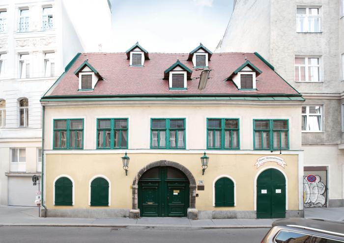 edificio amarillo con detalles verdes y techo rojo, entrada arqueada, buhardillas
