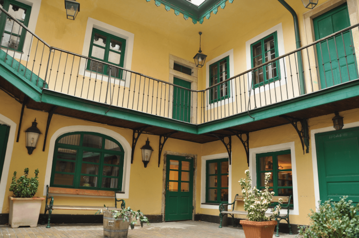edificio amarillo con contraventanas verdes y balcón en un patio