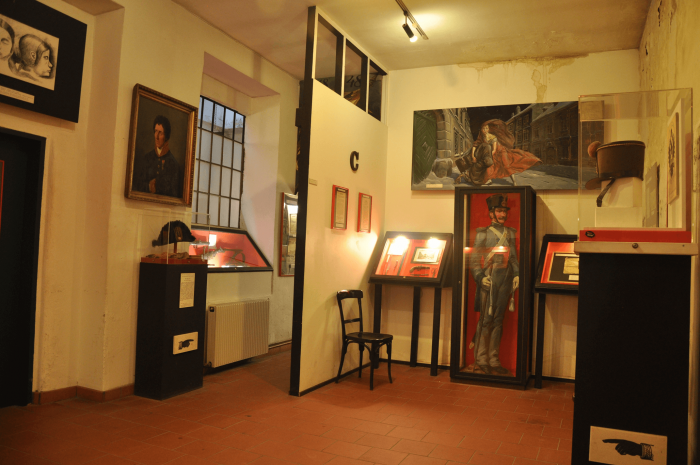 Interior de un museo con vitrinas, cuadros enmarcados y una gran pintura en la pared
