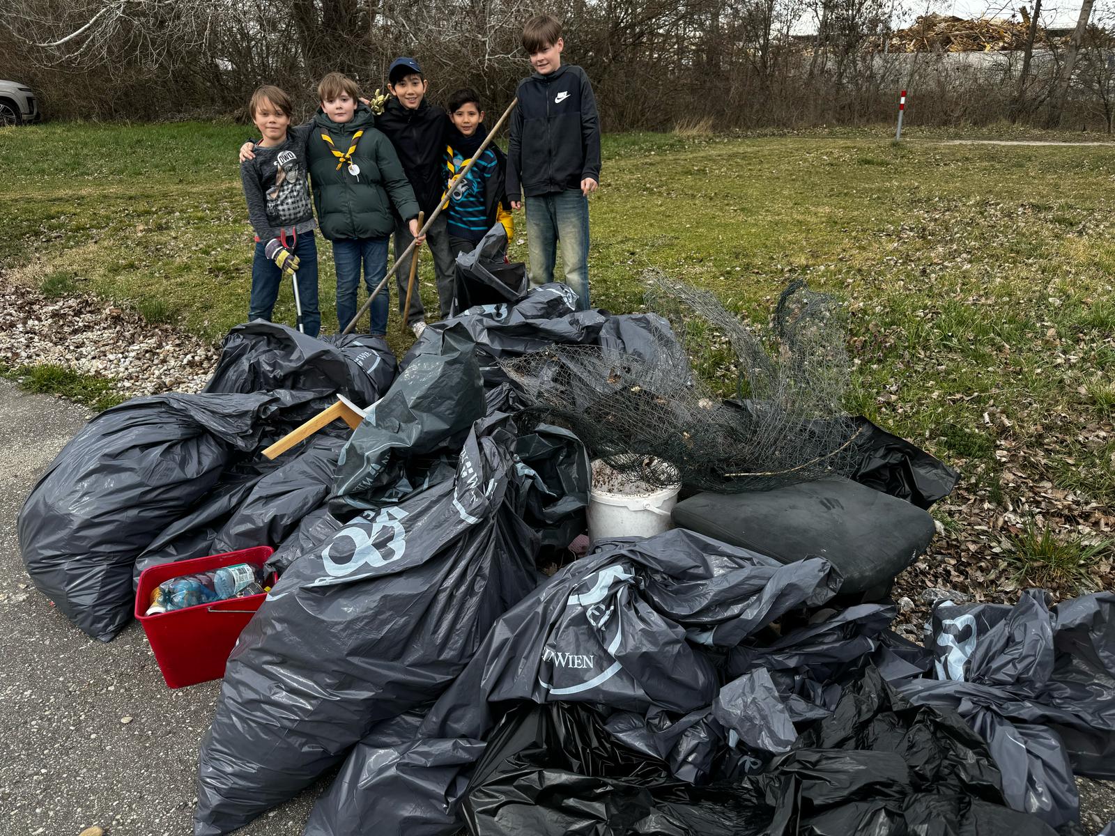niños y un adulto con cañas de pescar y bolsas de basura en una zona de césped