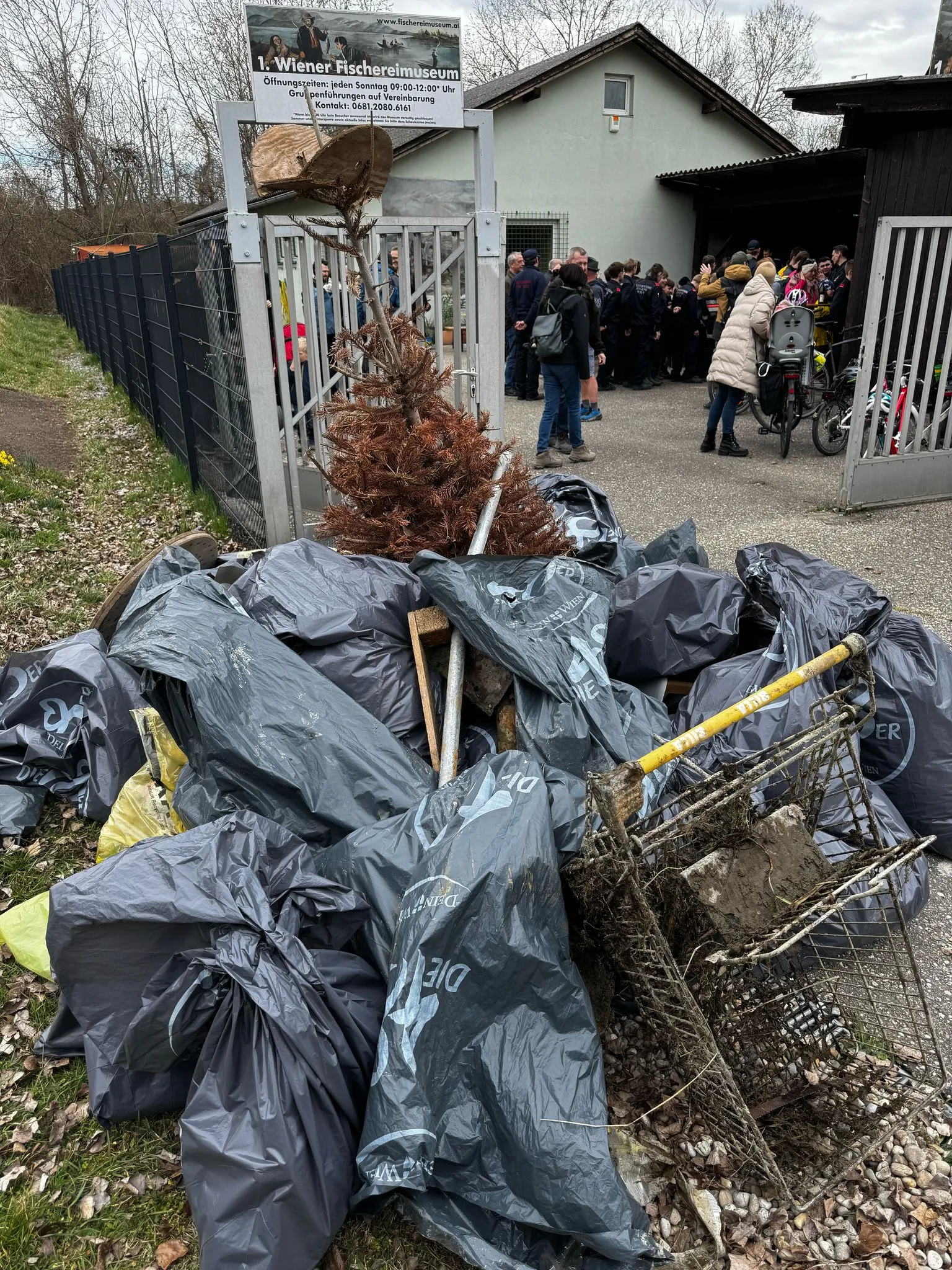 Pile of black trash bags and fishing equipment outside the Vienna Fisheries Museum entrance with people nearby