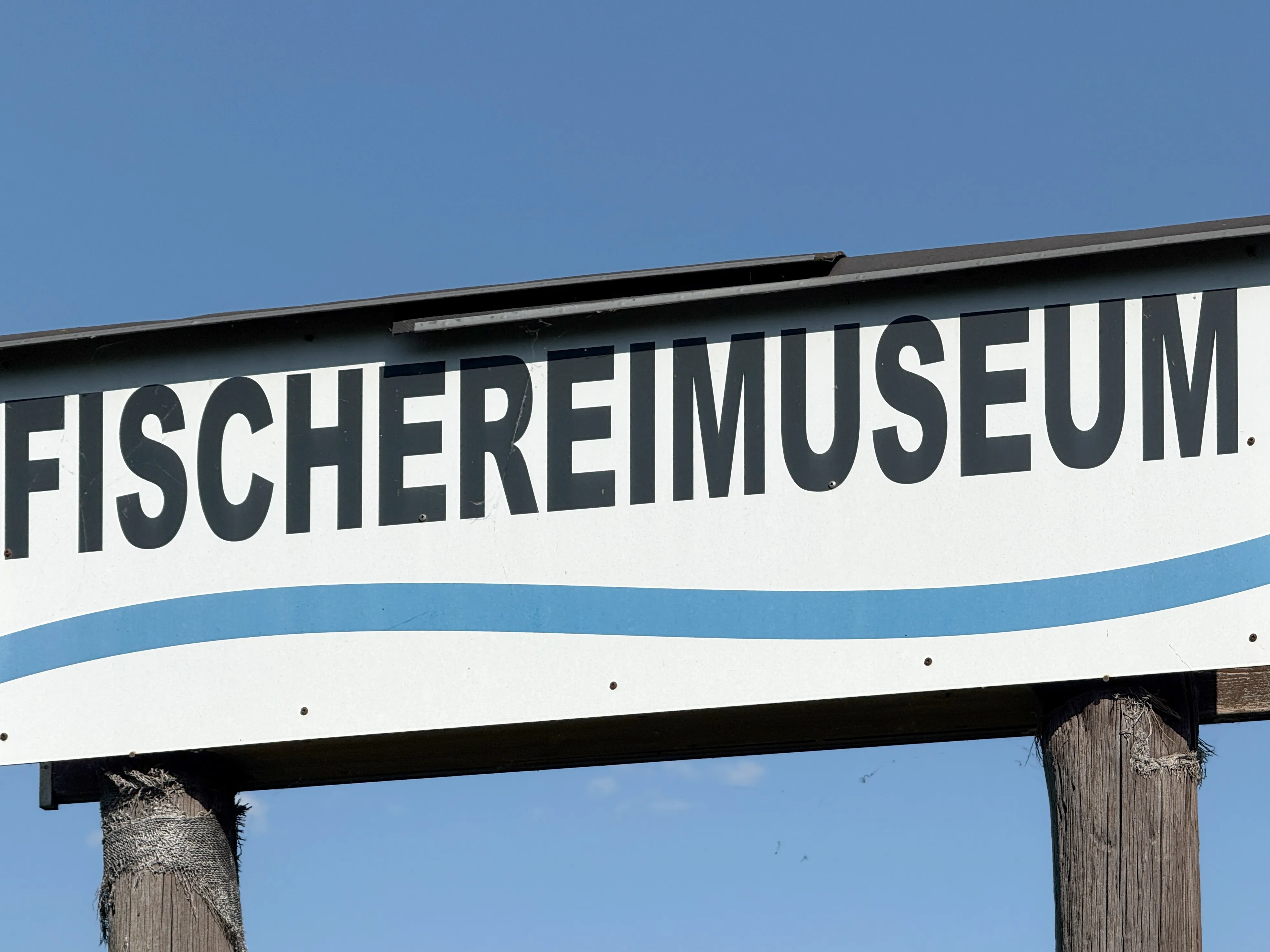Señal blanca con texto negro FISCHEREIMUSEUM y diseño de ola azul