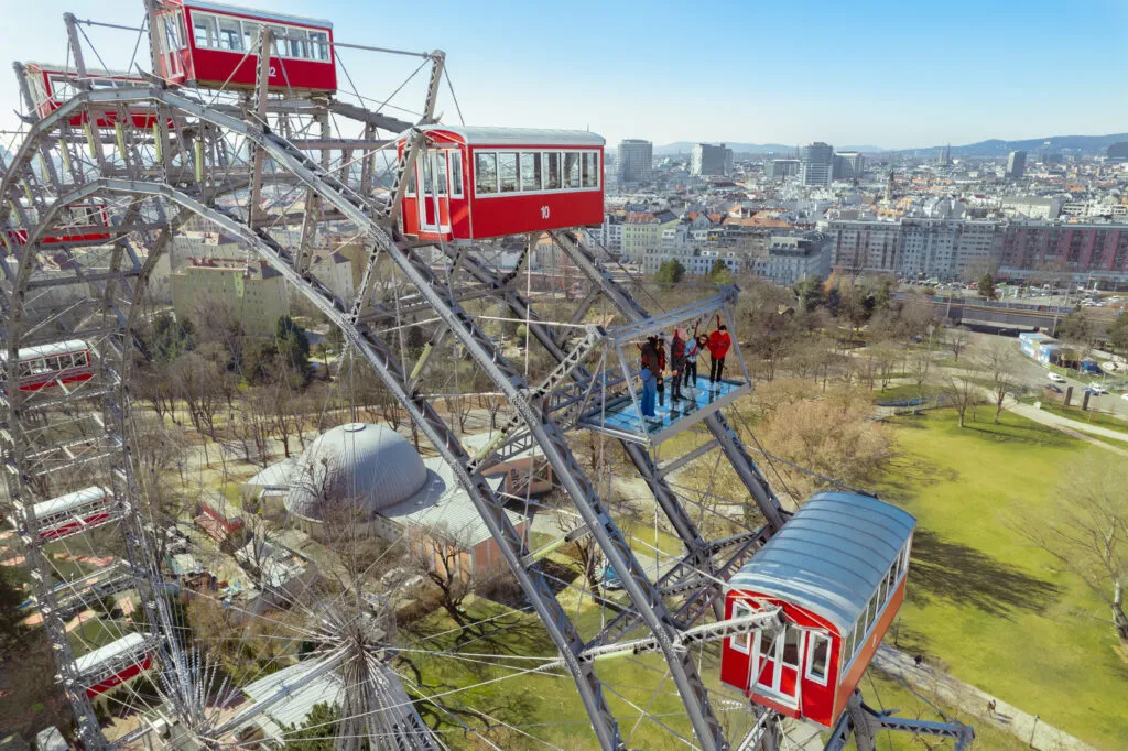 Czerwone kabiny Wiedeńskiego diabelskiego młyna na metalowej konstrukcji z panoramą miasta w tle