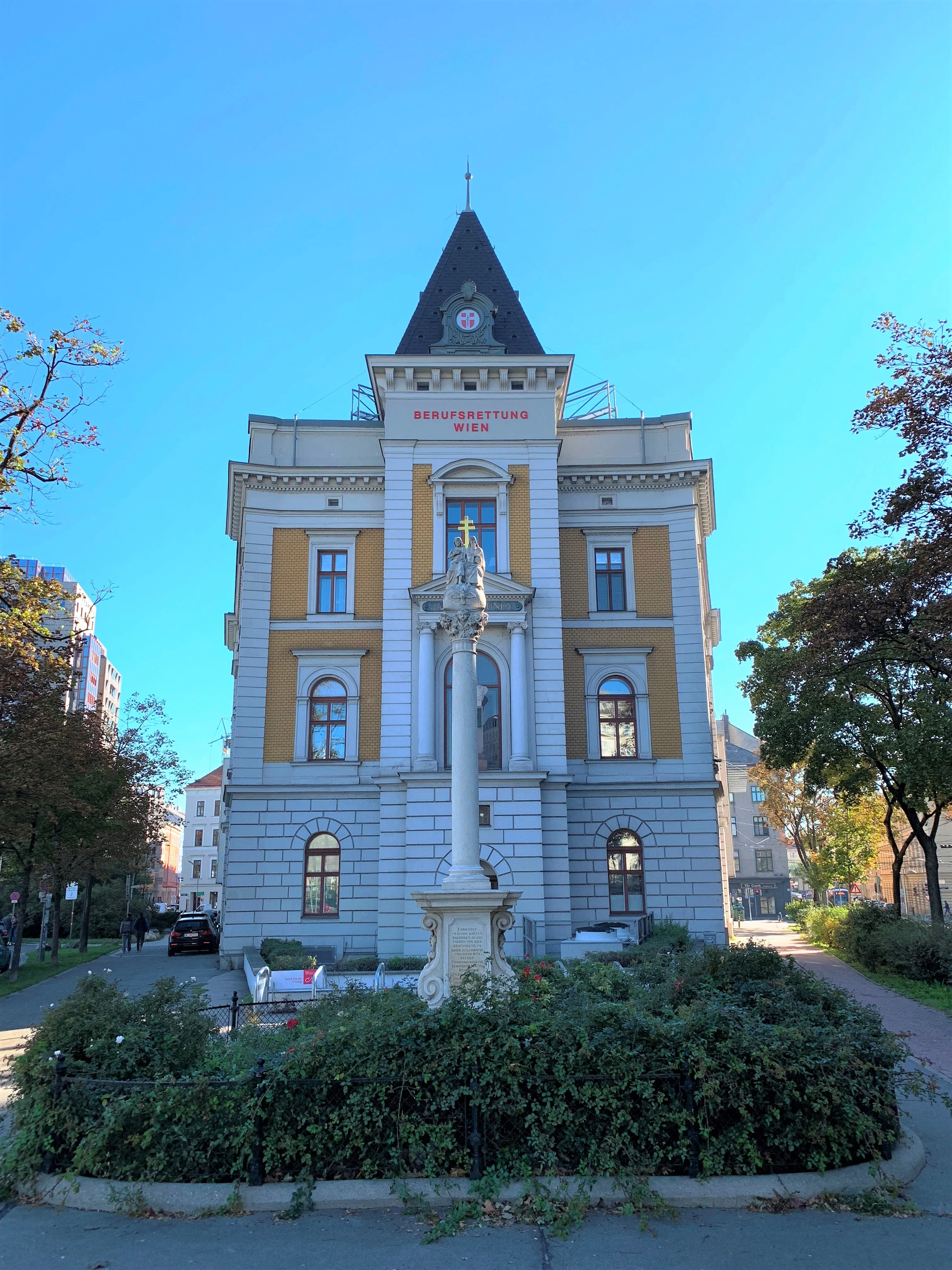 edificio histórico con fachada amarilla y blanca, torre y estatua delante, bajo un cielo azul claro
