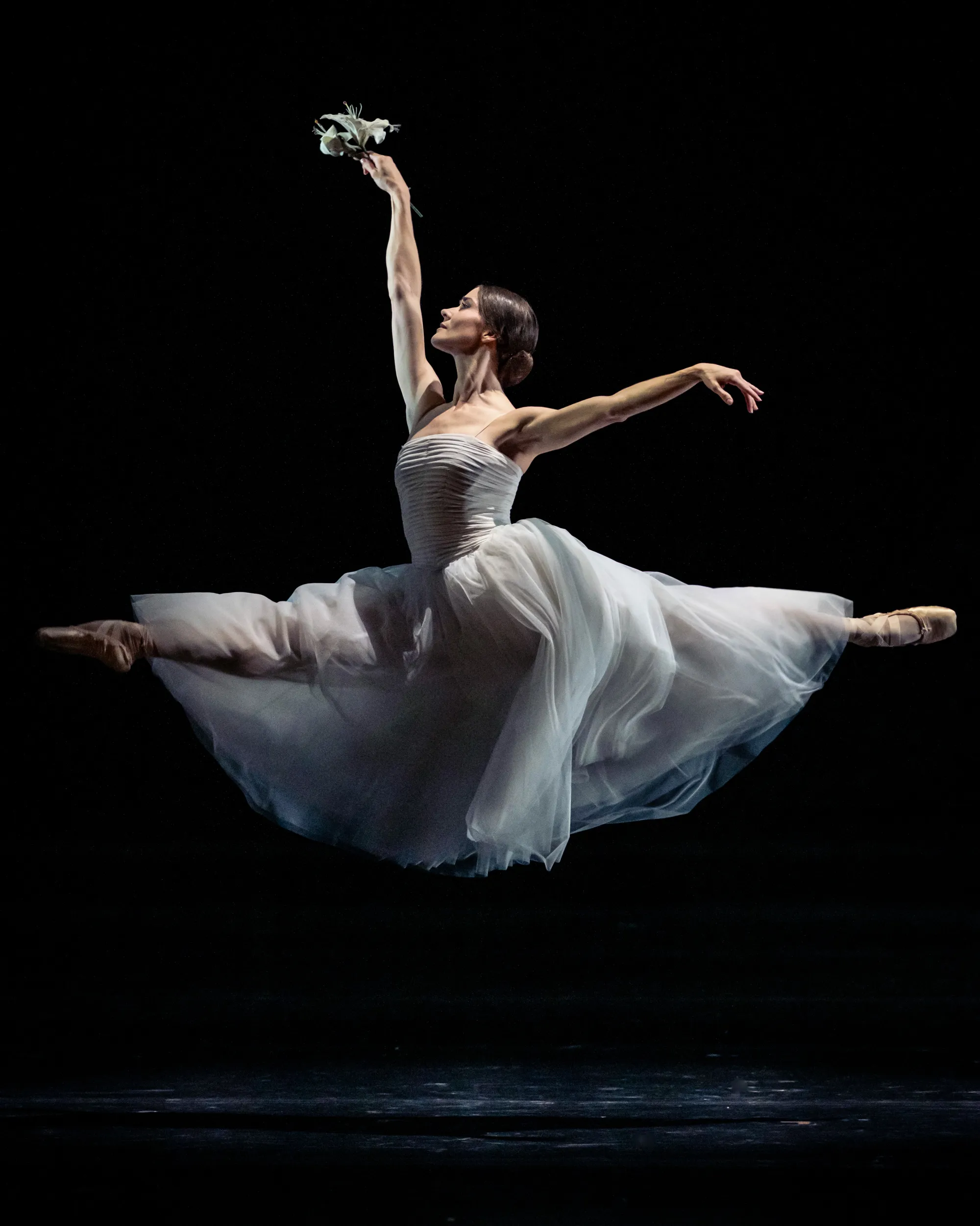 Een ballerina in een witte jurk die een sprong op het podium uitvoert