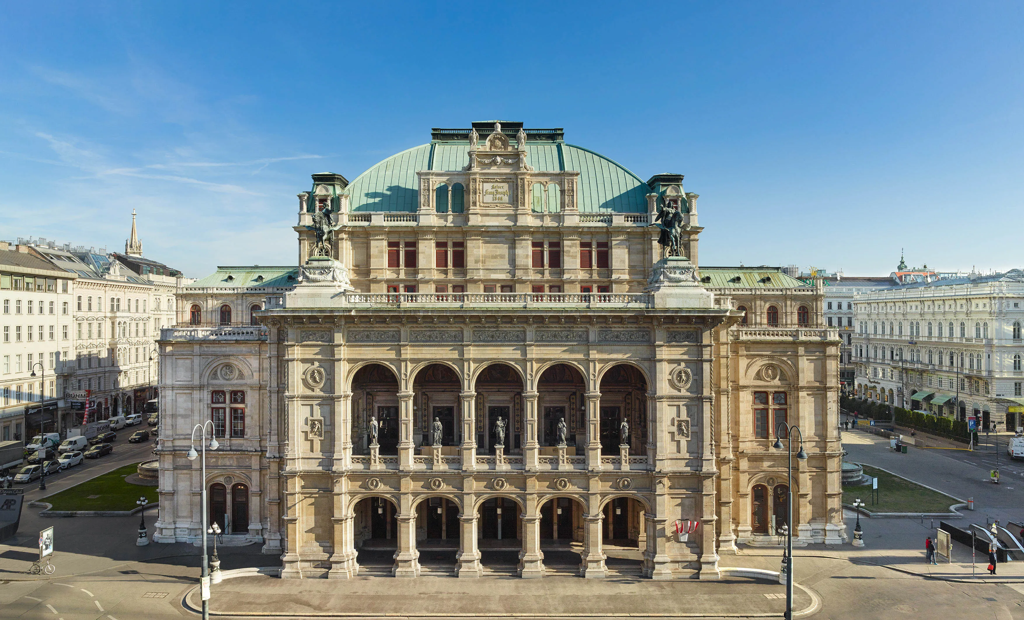 Grand neoclassicistisch gebouw met een groene koepel en boogvormige colonnades op een zonnige dag