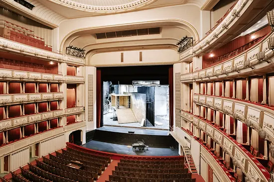 Ornate interieur van de Weense Staatsopera met rode stoelen, meerdere balkons en een podium