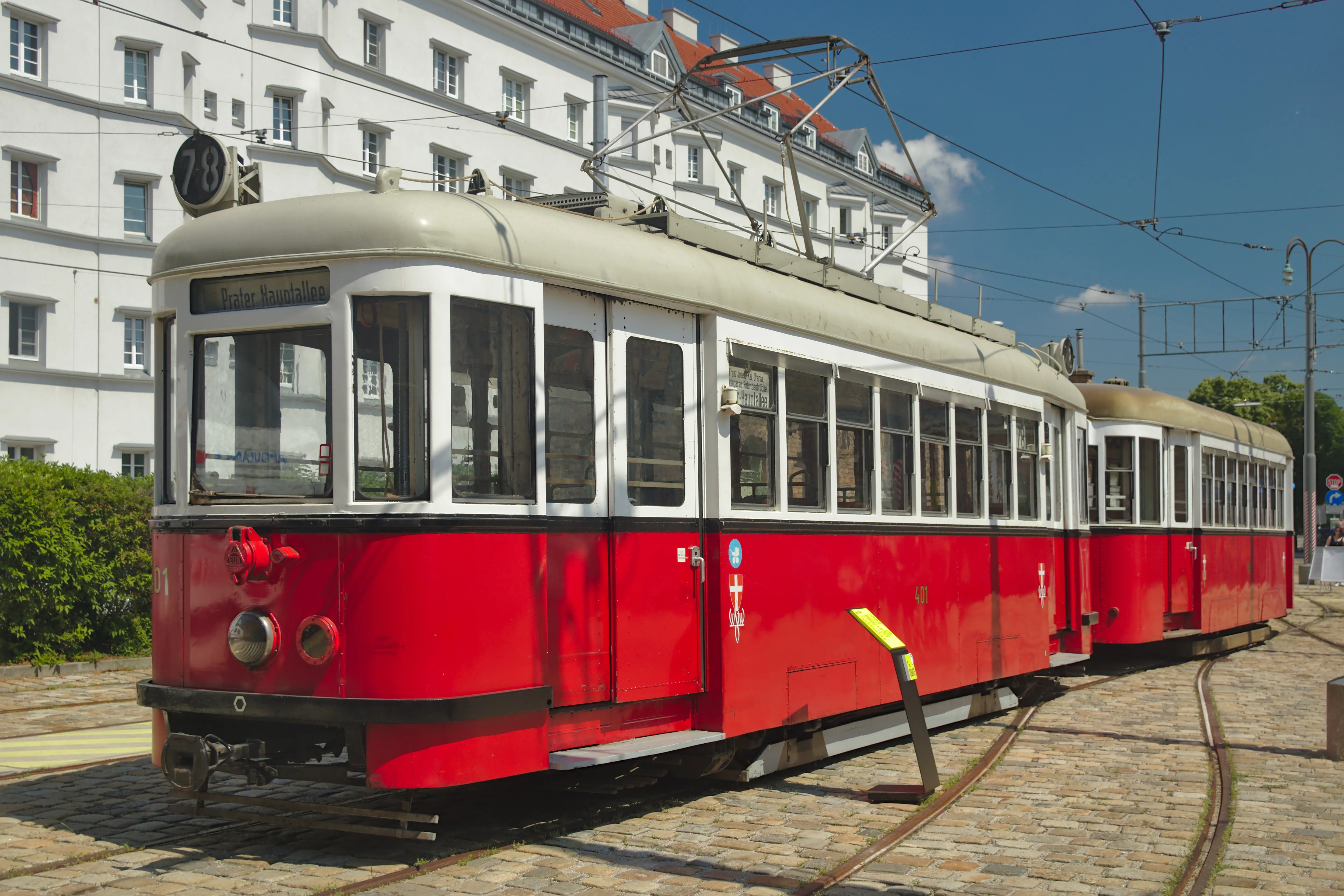 Czerwony i kremowy zabytkowy tramwaj na torach przed budynkiem