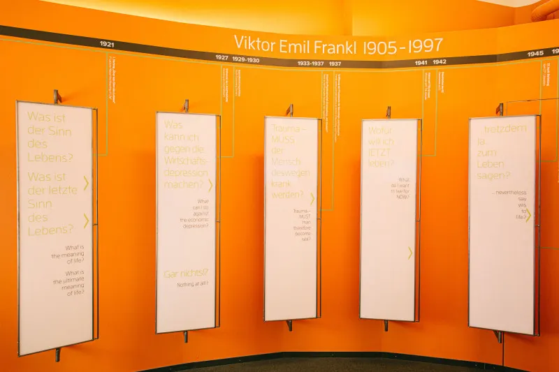 Pared curva naranja con paneles blancos que exhiben texto sobre Viktor Emil Frankl 1905-1997