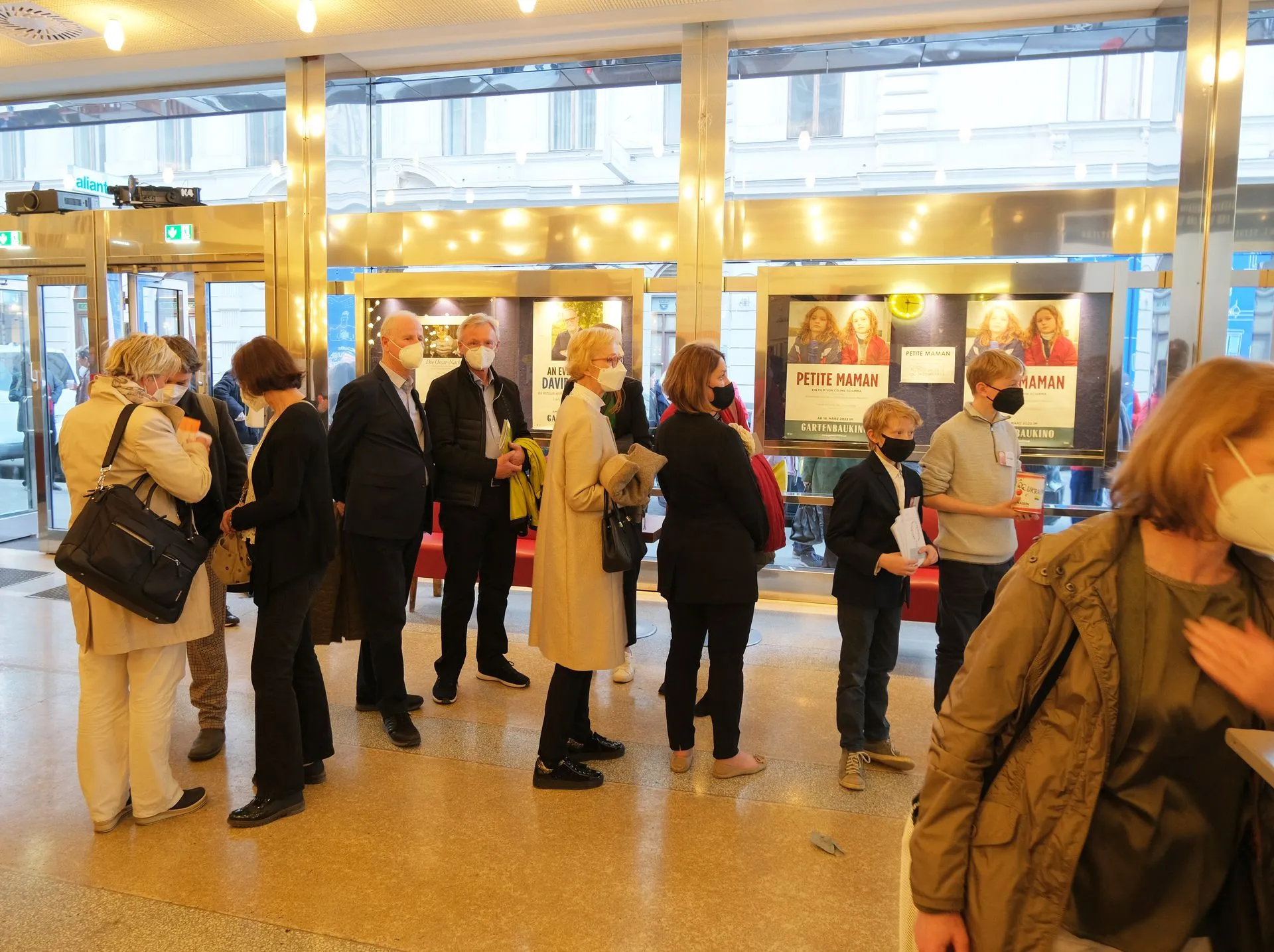 Personas de pie en el vestíbulo de un museo con carteles expuestos tras puertas de cristal