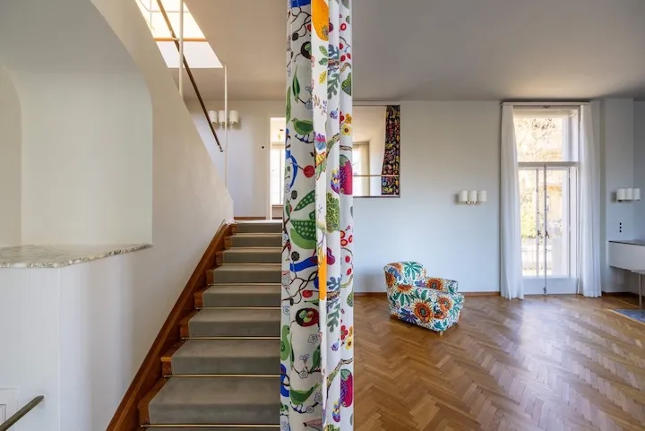 Interior de Villa Beer con una columna de azulejos de colores, una escalera de madera y un sillón floral