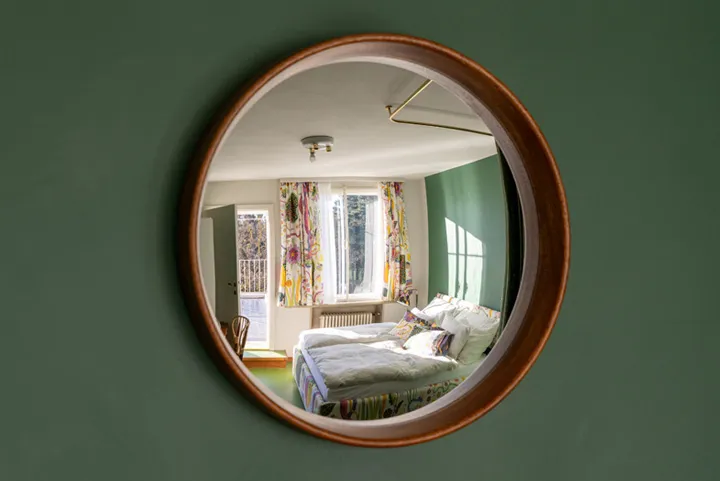Espejo circular que refleja un dormitorio con cortinas estampadas y una cama
