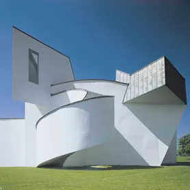 Biały dekonstruktywistyczny budynek o zakrzywionych i kanciastych betonowych formach na tle błękitnego nieba, Vitra Design Museum projektu Franka Gehry'ego