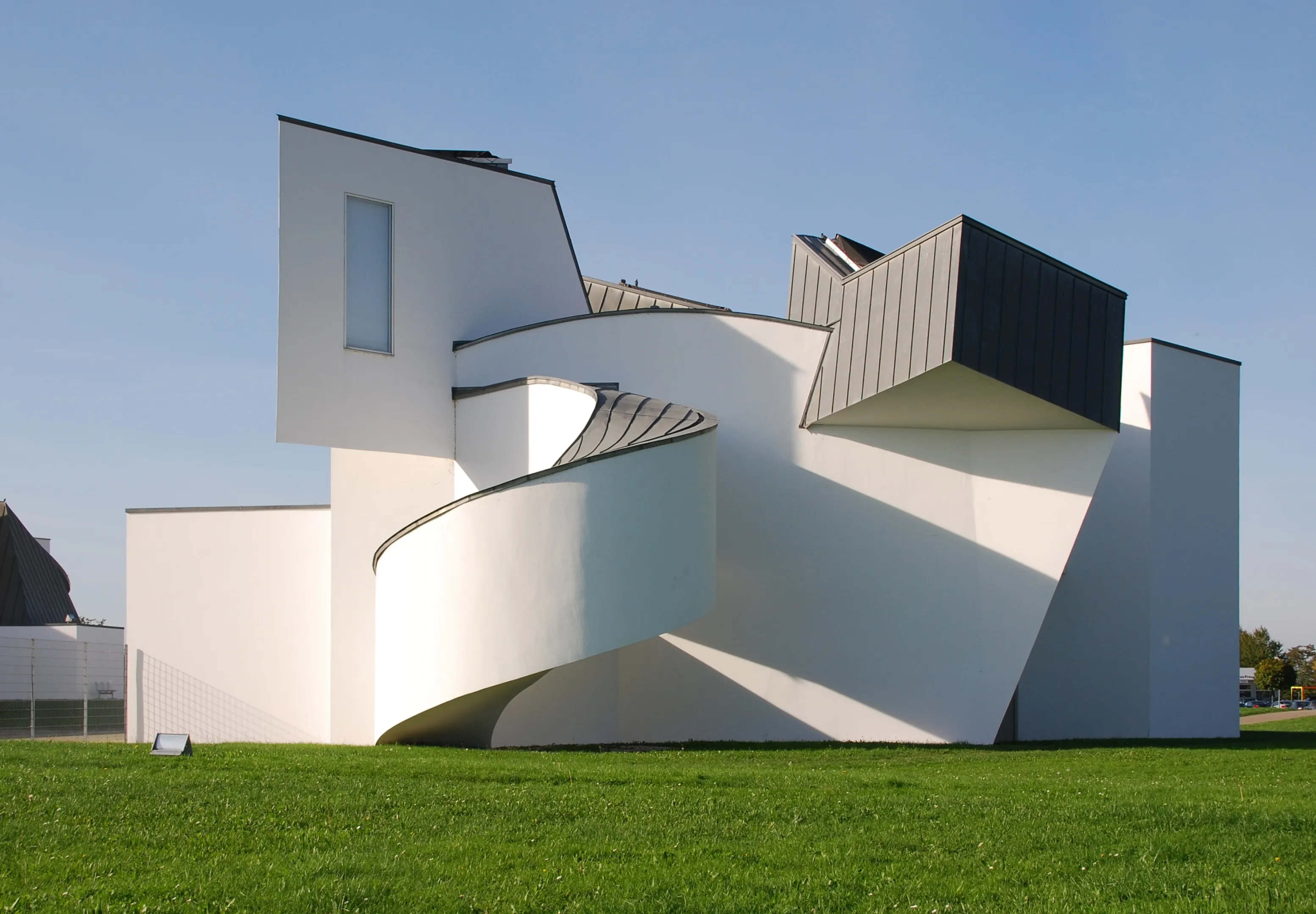 Wit deconstructivistisch museumgebouw met gebogen en hoekige geometrische vormen op een groen gazon onder een helderblauwe lucht