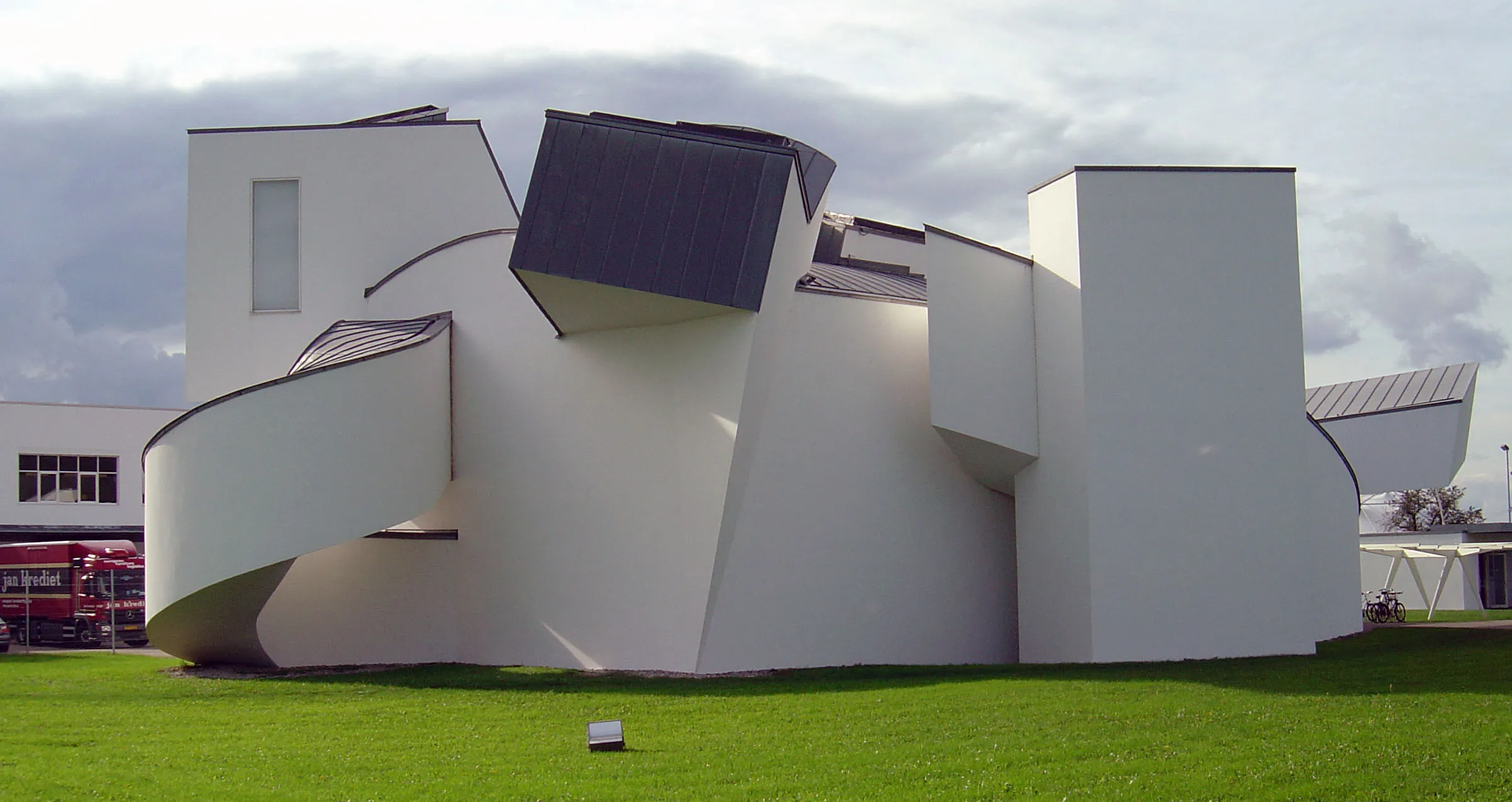 Wit deconstructivistisch museumgebouw met gebogen en hoekige geometrische vormen op een groen gazon onder een bewolkte hemel