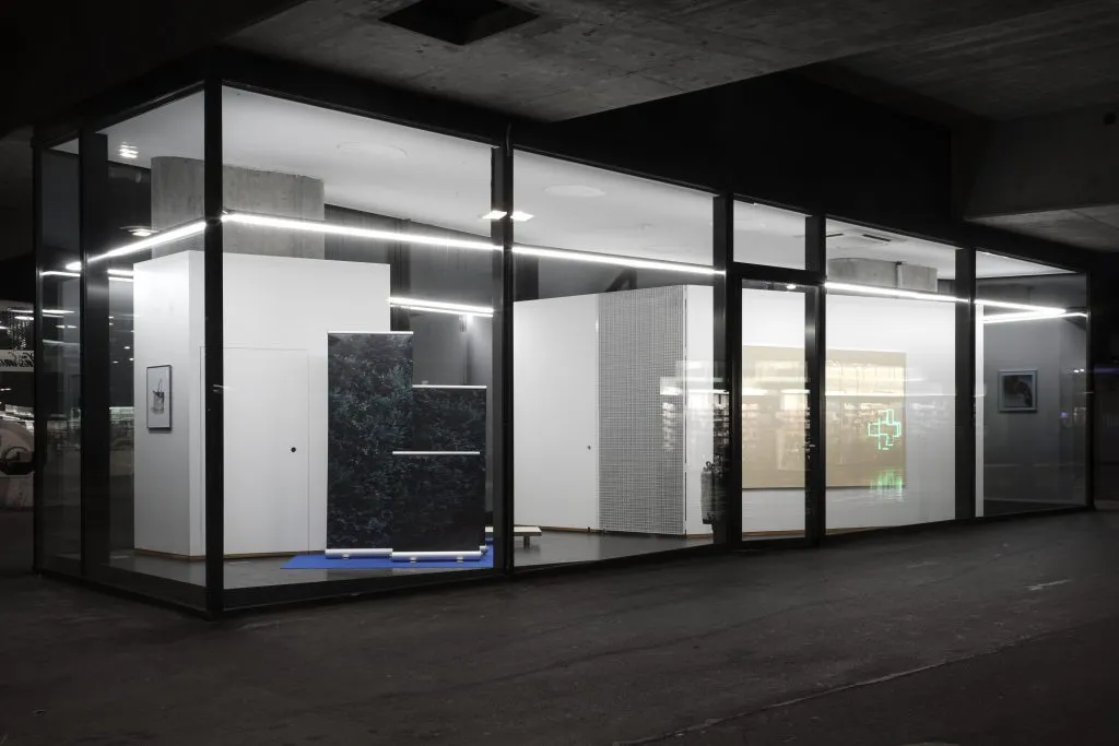 Szklana przestrzeń wystawowa w nocy, z oświetleniem wnętrza podkreślającym białe ściany galerii i instalacjami artystycznymi widocznymi przez przezroczystą fasadę