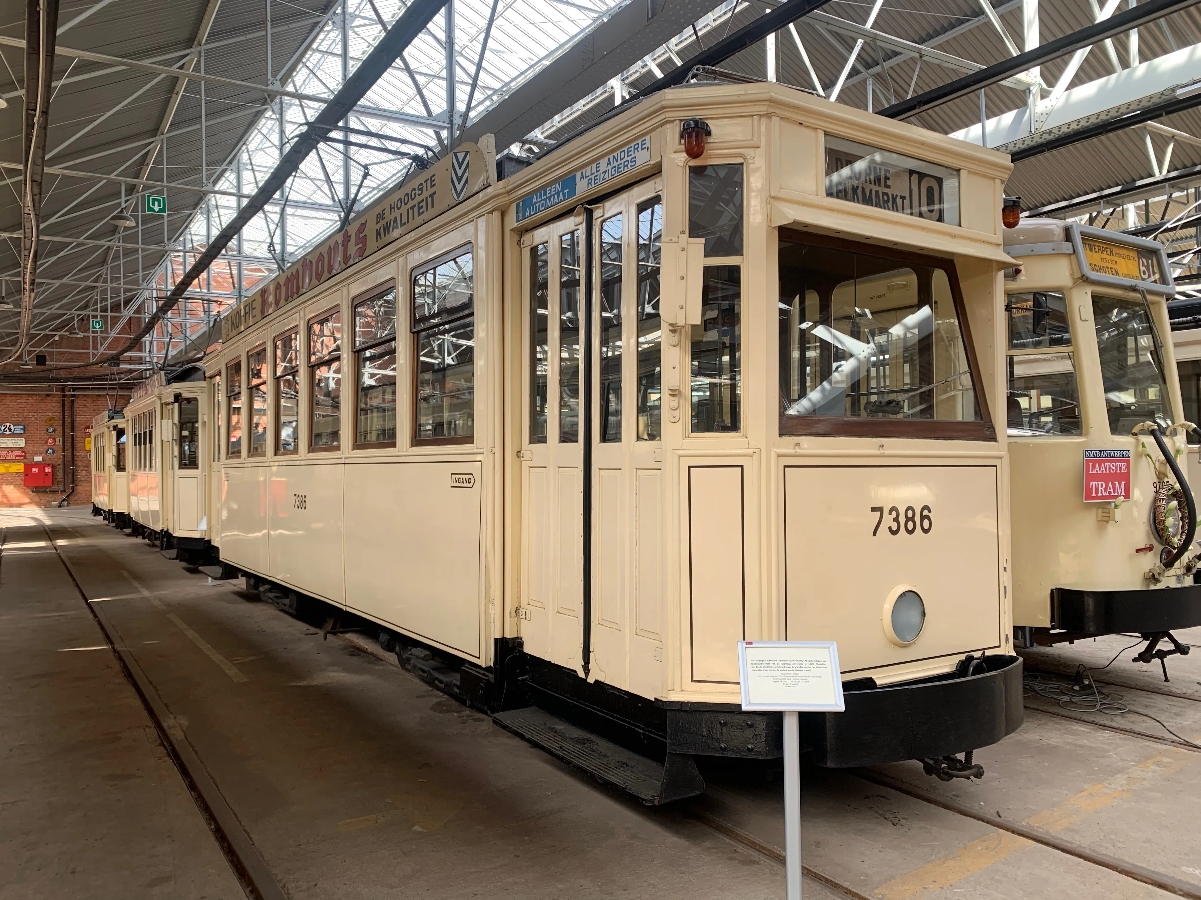 Kremowy zabytkowy tramwaj numer 7386 wyeksponowany w dużej hali muzealnej z metalowymi wiązarami dachowymi i torami tramwajowymi