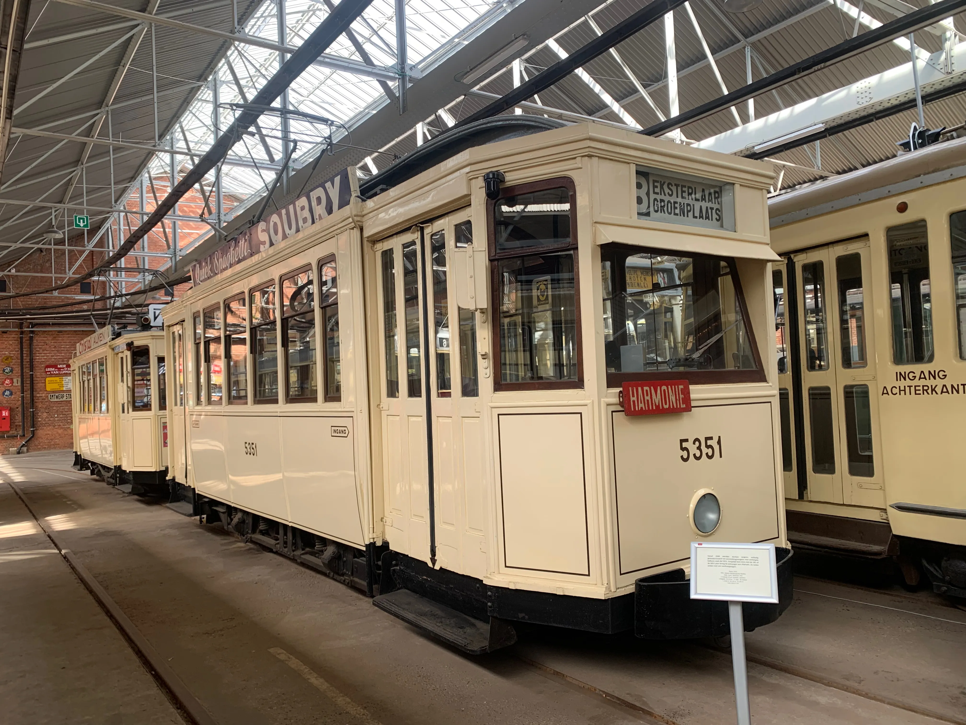 Kremowy zabytkowy tramwaj numer 5351 z tablicą kierunkową Mortsel-Boekenberg Centrum, wyeksponowany w dużej hali muzealnej zajezdni tramwajowej obok innych zabytkowych tramwajów.