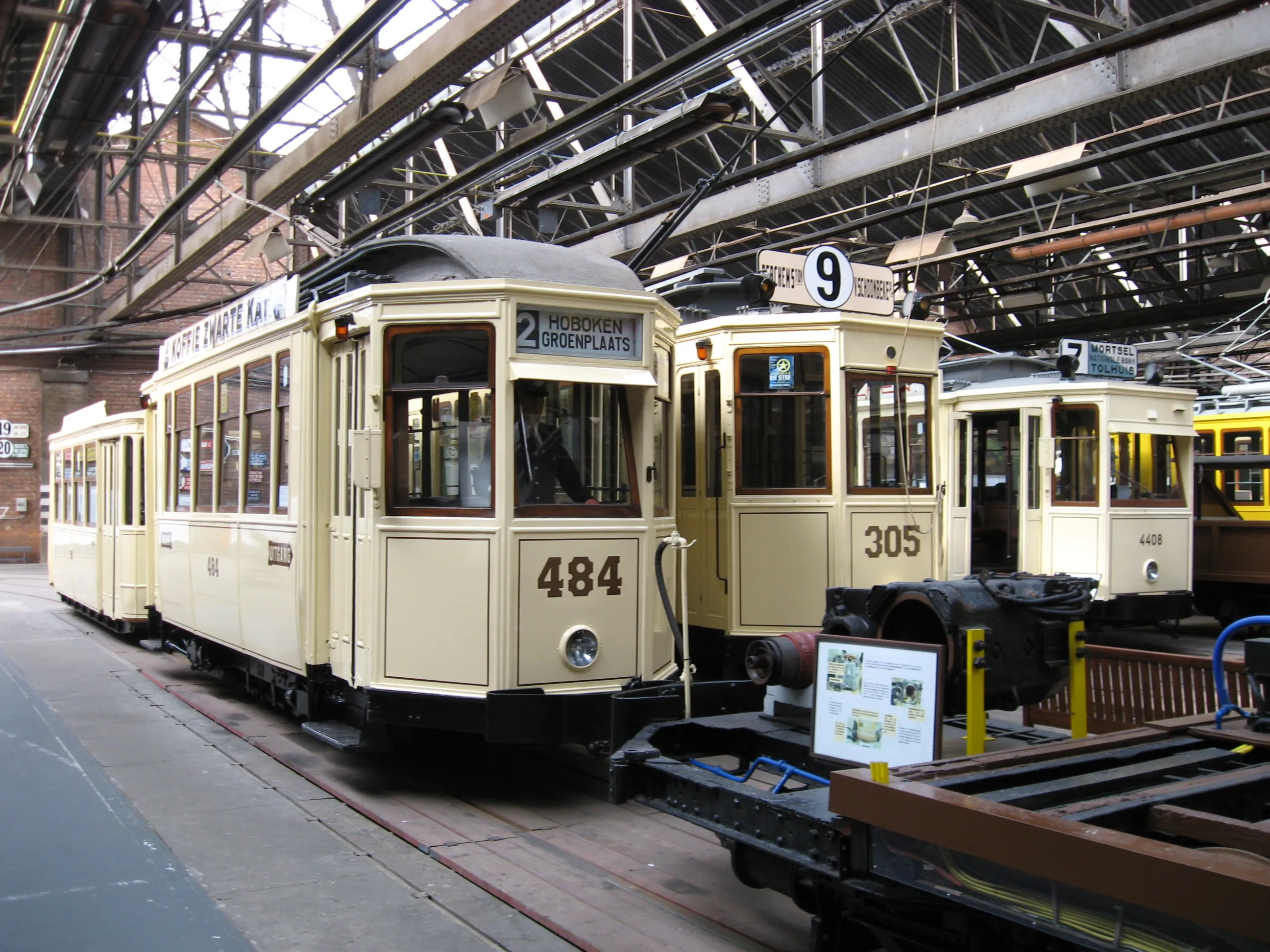 Históricos tranvías de color crema numerados 484 y 305 exhibidos dentro de una gran nave de ladrillo con estructura de acero en el Vlaams Tram- en Autobusmuseum