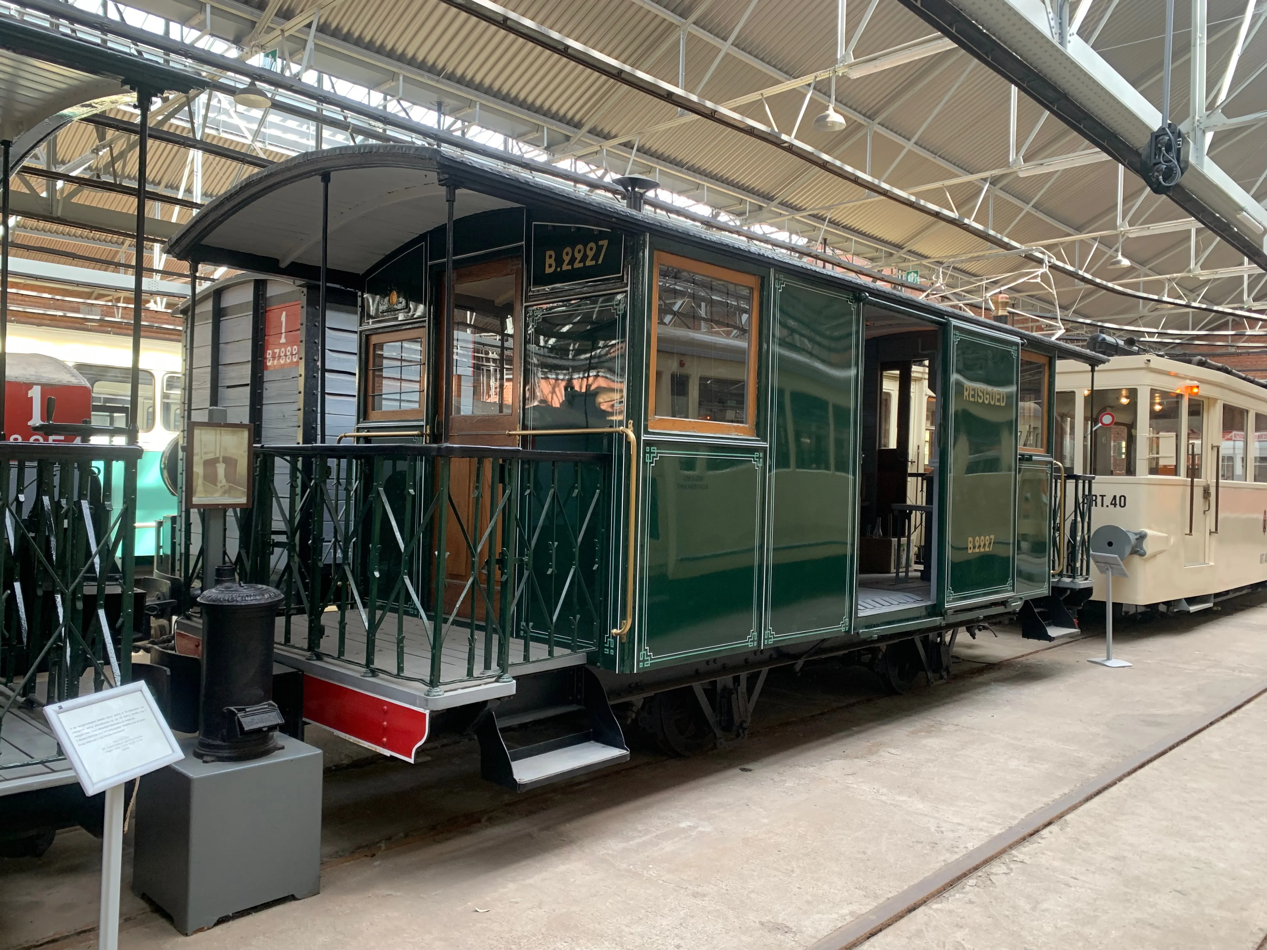Zabytkowy zielony tramwaj o numerze 257 wystawiony wewnątrz dużej zajezdni muzealnej, z otwartym tylnym pomostem, zielonymi barierkami i innymi zabytkowymi tramwajami widocznymi w tle.
