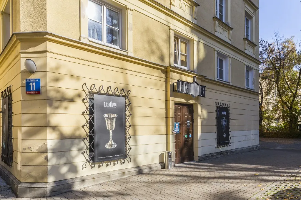 żółty budynek narożny z szyldem przedstawiającym kieliszek do wódki i słowem 'wódka' na czarnym tle