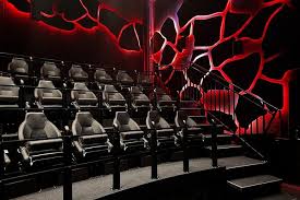 Rows of motion simulator seats in a dark room with red glowing volcanic crack designs on the walls.