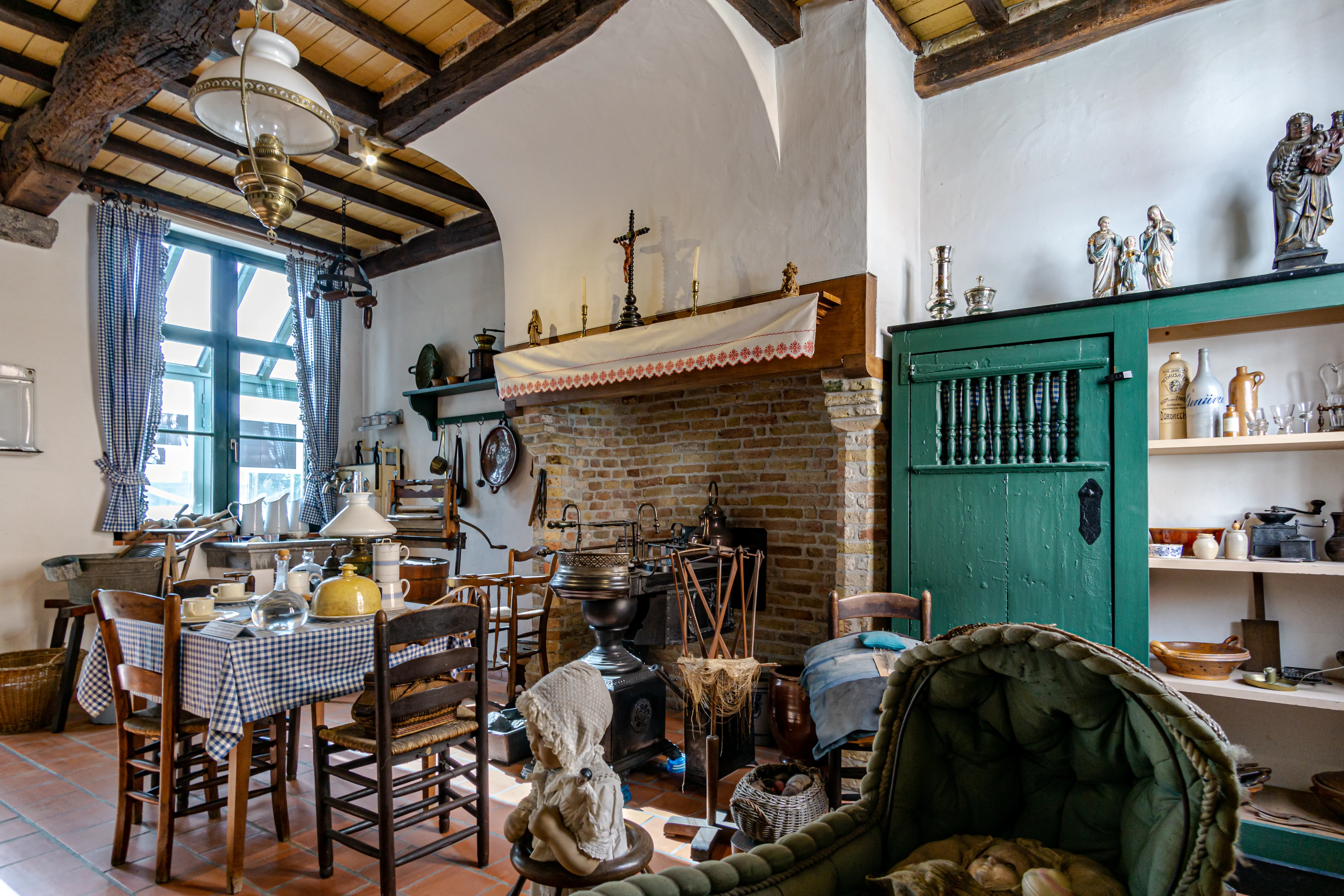 Interior del Volkskundemuseum que muestra una sala histórica recreada con techo de vigas de madera, chimenea de ladrillo, mesa de comedor con mantel a cuadros y un armario verde que exhibe objetos de época.