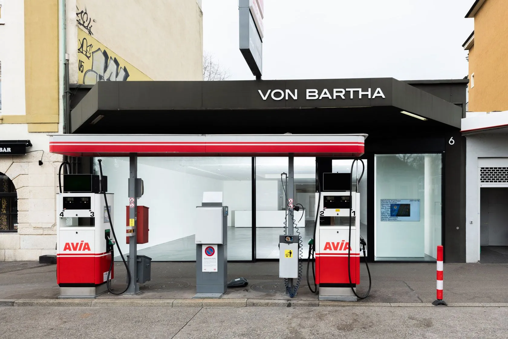 Exterior of von Bartha Basel gallery with black facade, red and white AVIA gas pumps in front, and large glass windows