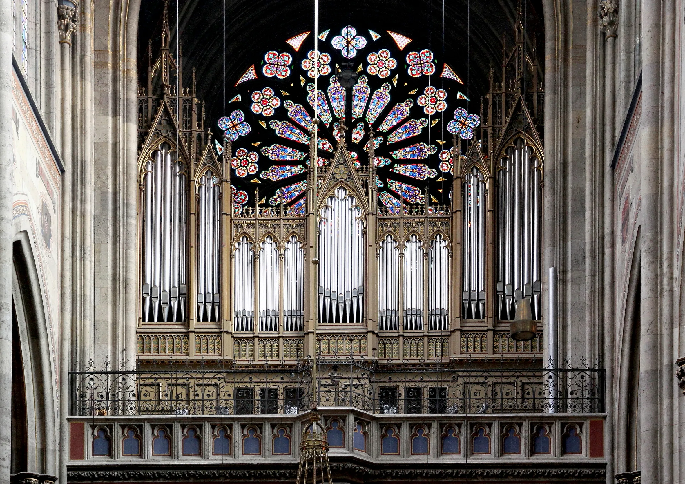 A large pipe organ beneath a colorful stained glass rose window inside a gothic church.