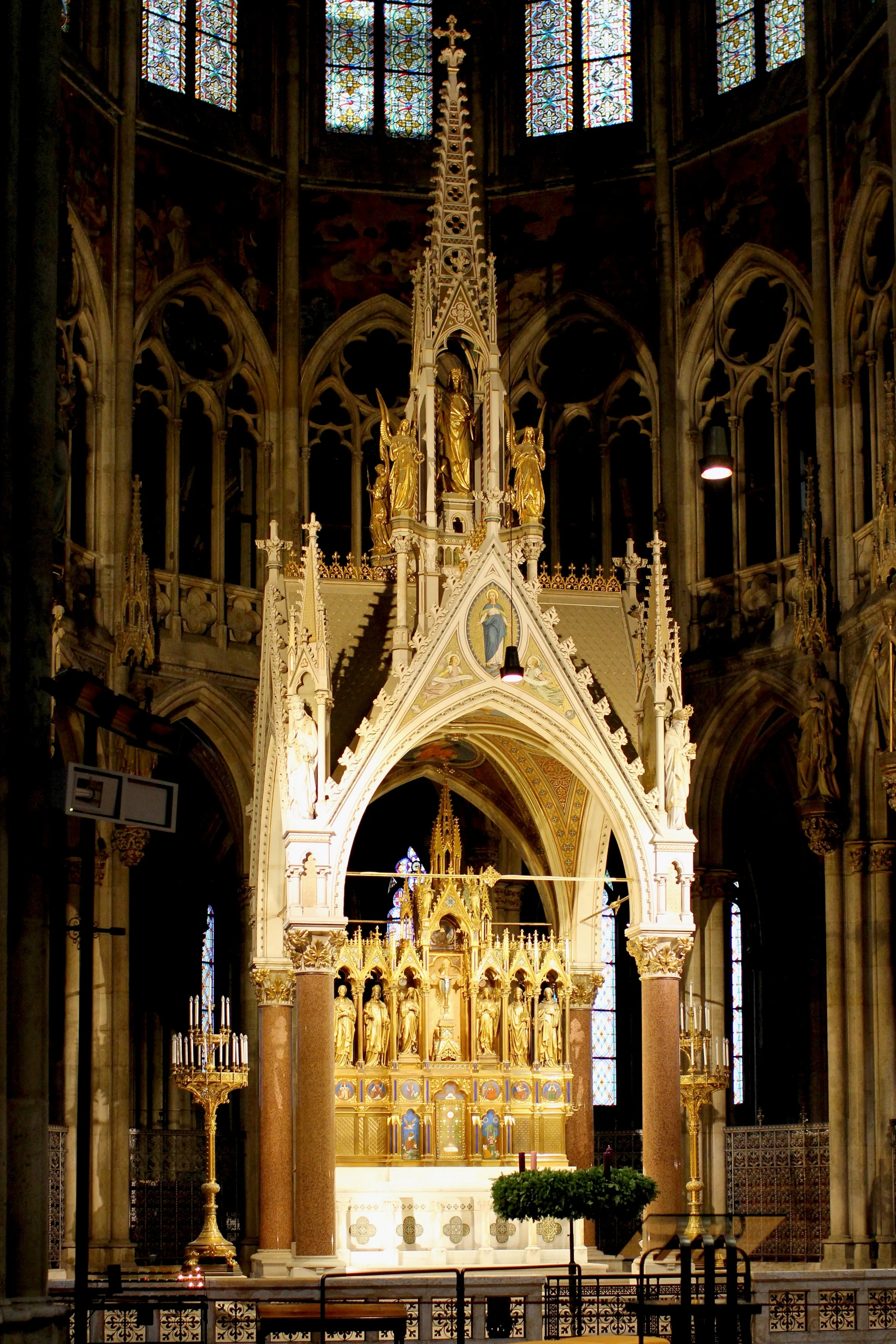 Interior of the Votive Church showing a grand high altar with golden statues, pointed arches, and stained glass windows.