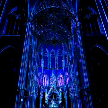 Interior of a neo-Gothic church with blue lighting, tall columns, and stained glass windows