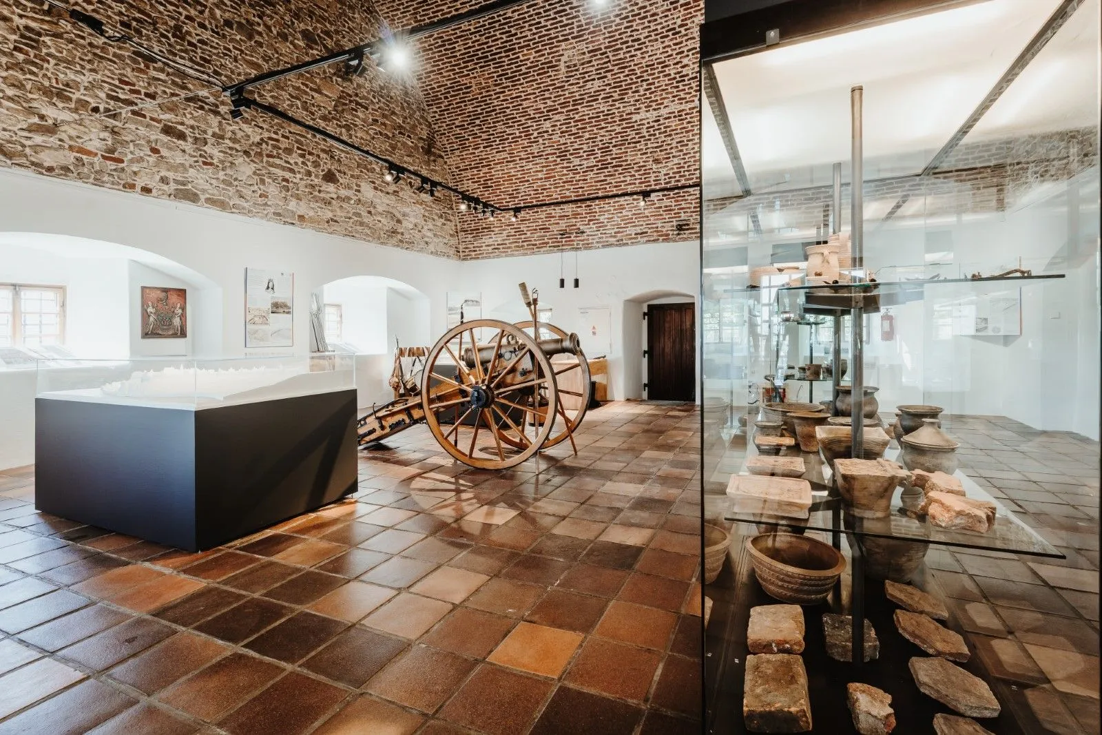 Interior de un museo con una rueda de madera, vitrinas y paredes de ladrillo