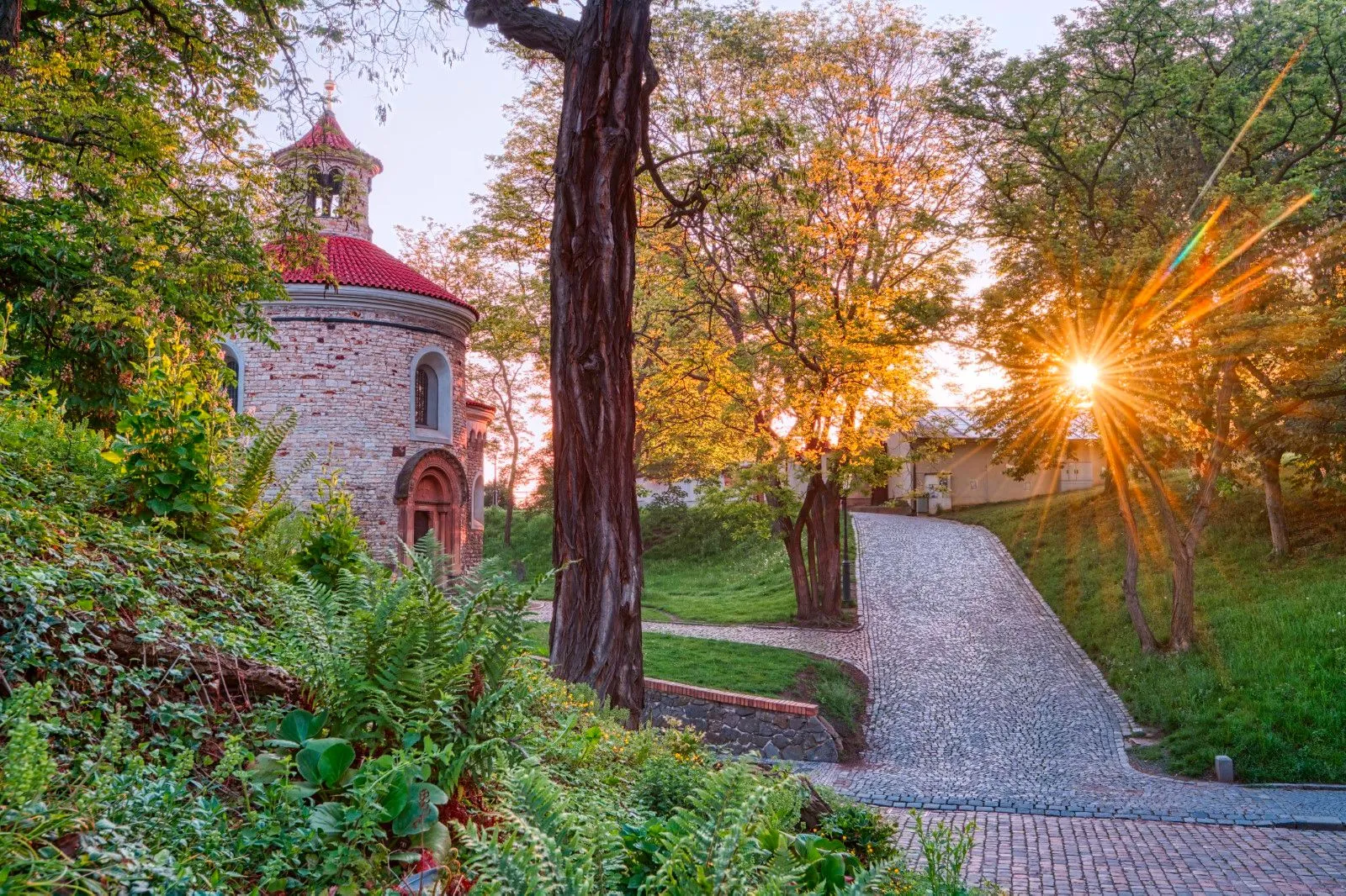 edificio de piedra con techo rojo rodeado de árboles y vegetación al atardecer