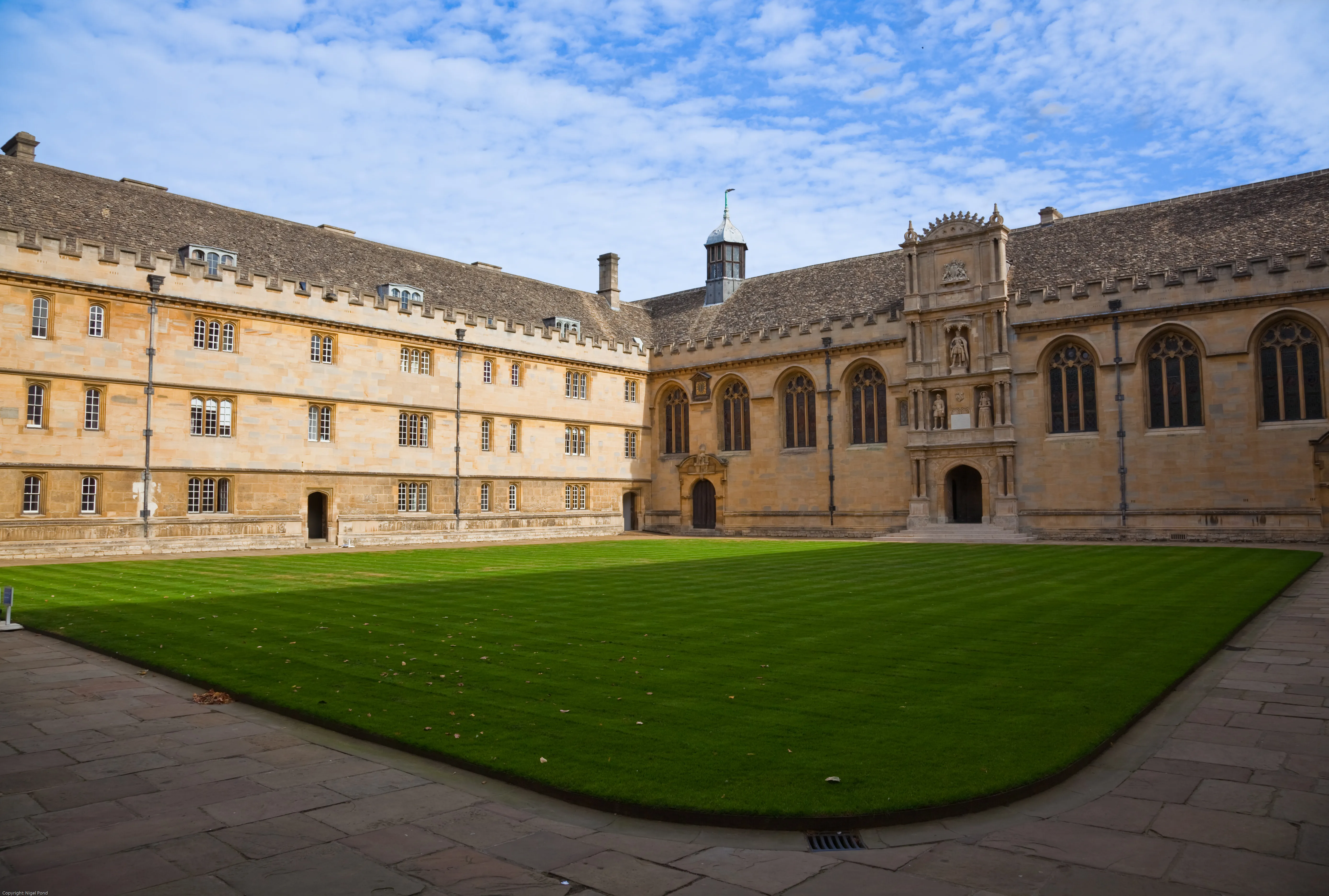 Szeroki widok na przedni dziedziniec Wadham College z dużym, prostokątnym trawnikiem otoczonym zabytkowymi budynkami z kamienia w stylu jakubowym, z gotyckimi oknami i ozdobną fasadą wejściową.