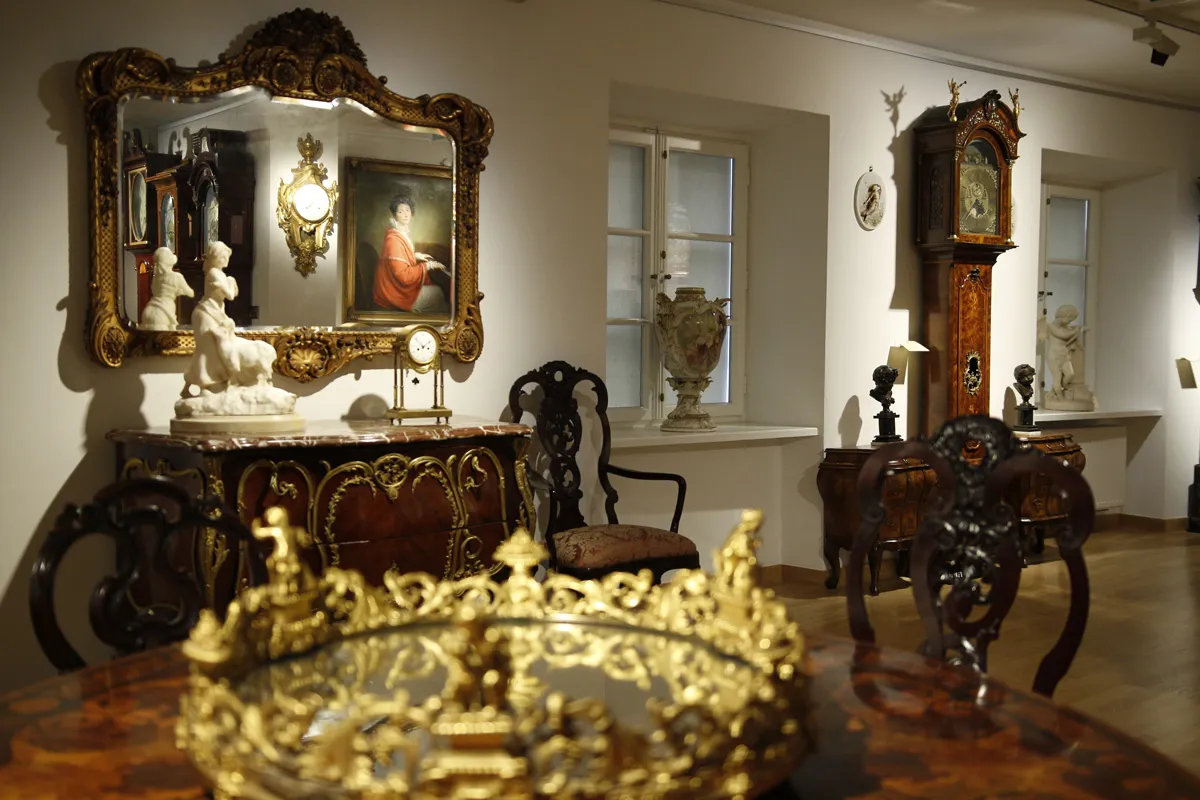 Sierlijk houten meubilair, een vergulde spiegel, een portretschilderij en een hoge houten klok in een museumgalerij