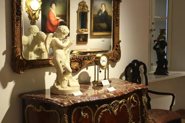 Marmeren cherubijnbeeldje op een gesneden houten kabinet met verguld spiegel en portretten op de achtergrond