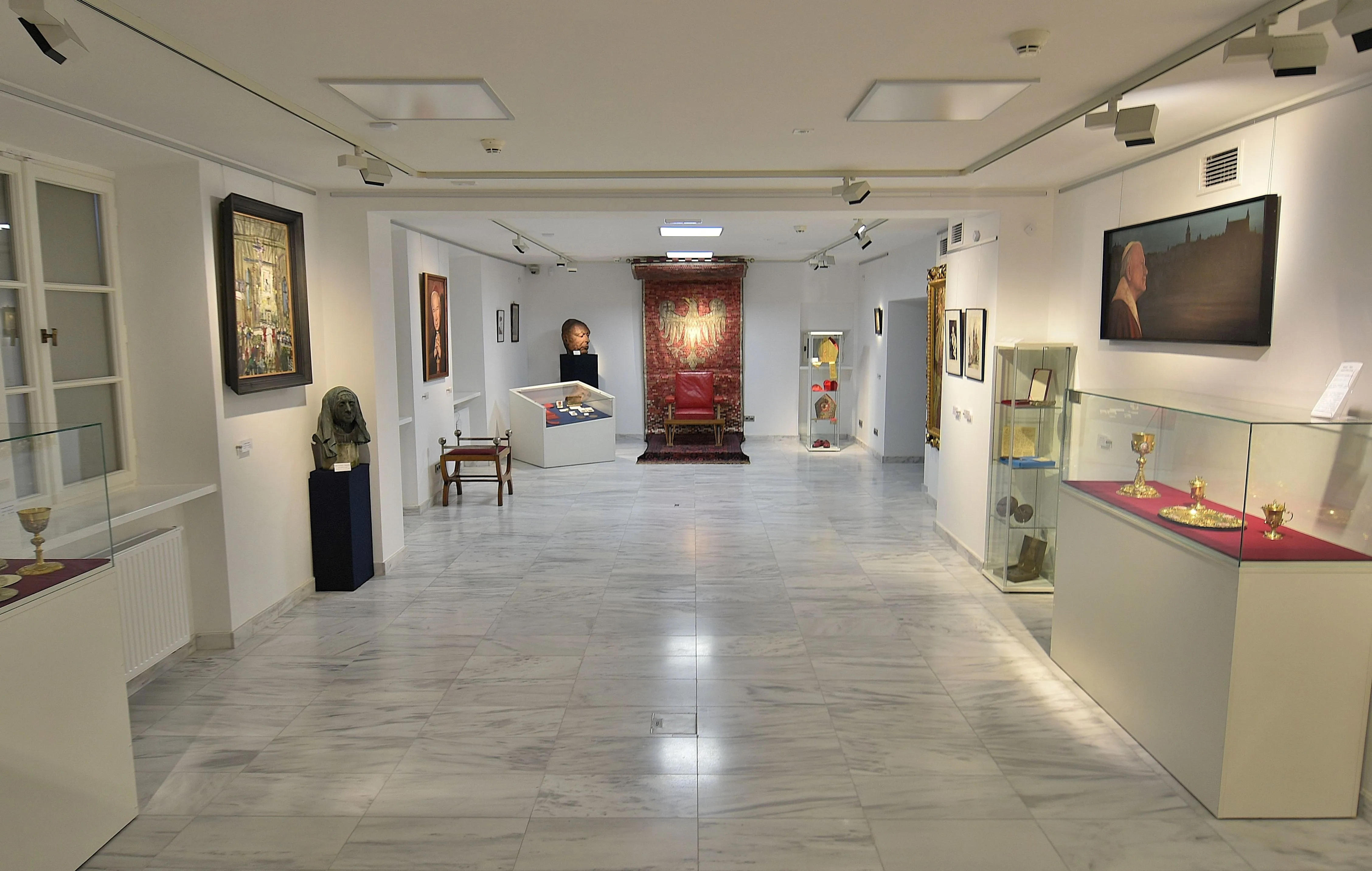Interieur van een gang in een museum met witte marmeren vloeren, vitrines en ingelijste kunstwerken aan de muren
