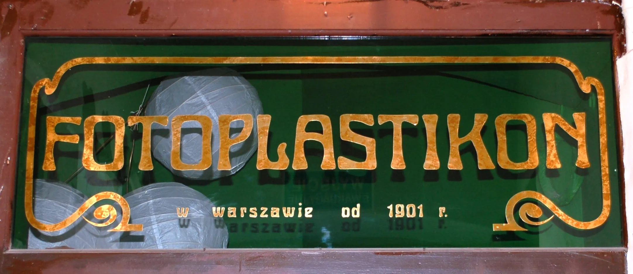 Un letrero verde con letras doradas que dice 'FOTOPLASTIKON w warszawie od 1901 r.'