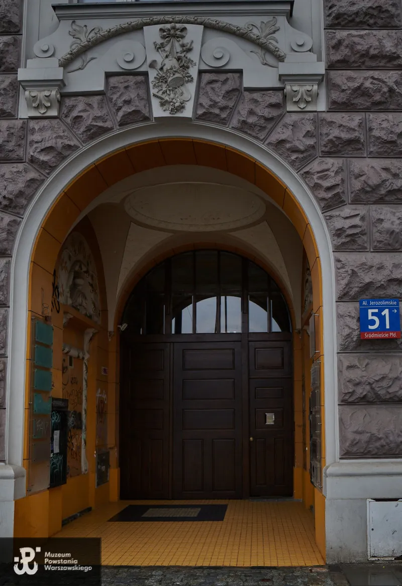 Stone building entrance with an arched doorway, ornate stonework, and a blue street sign reading '51' on the right.