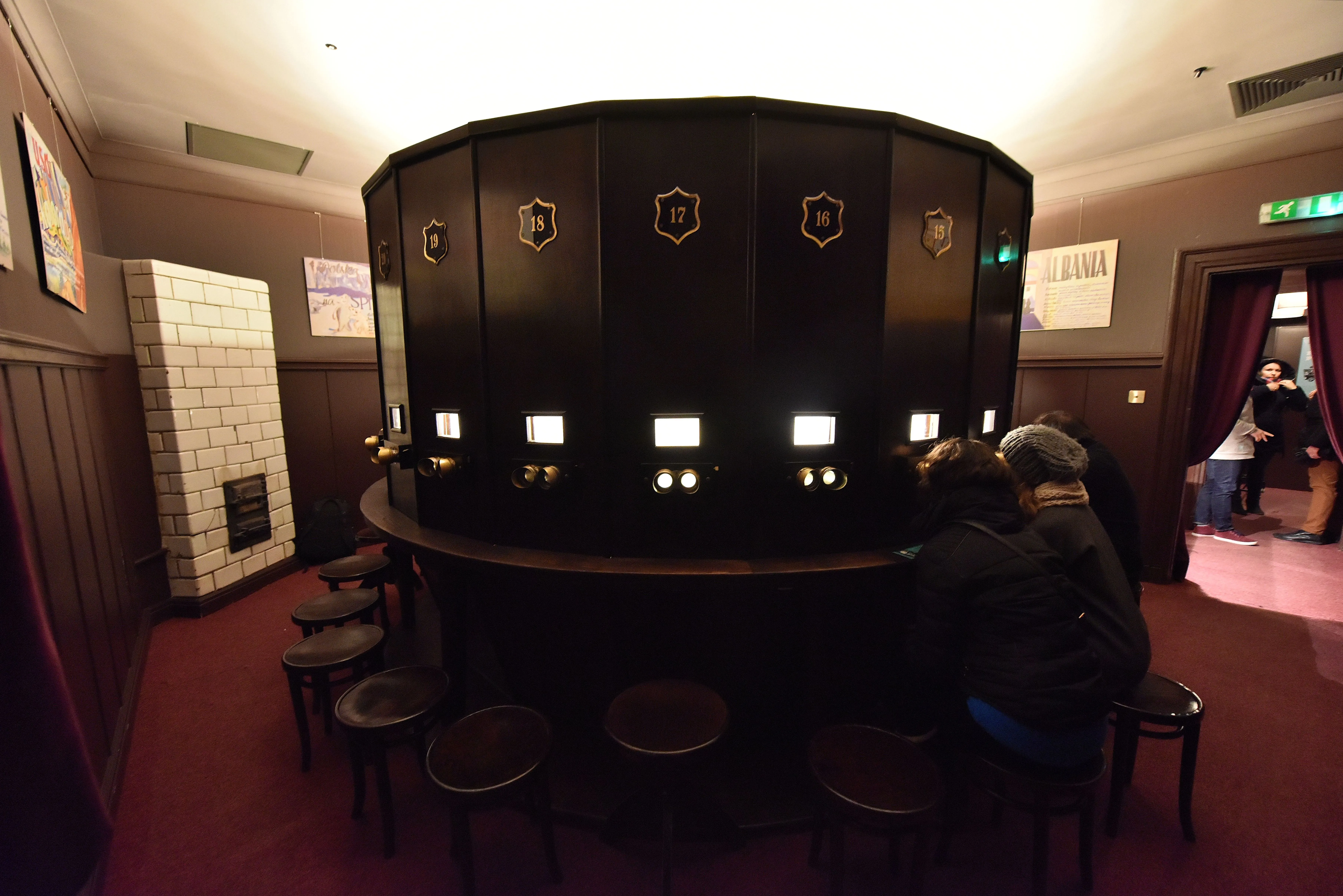 Interior del Fotoplastikon de Varsovia con una cabina de observación circular, personas sentadas en taburetes y un ambiente de sala vintage