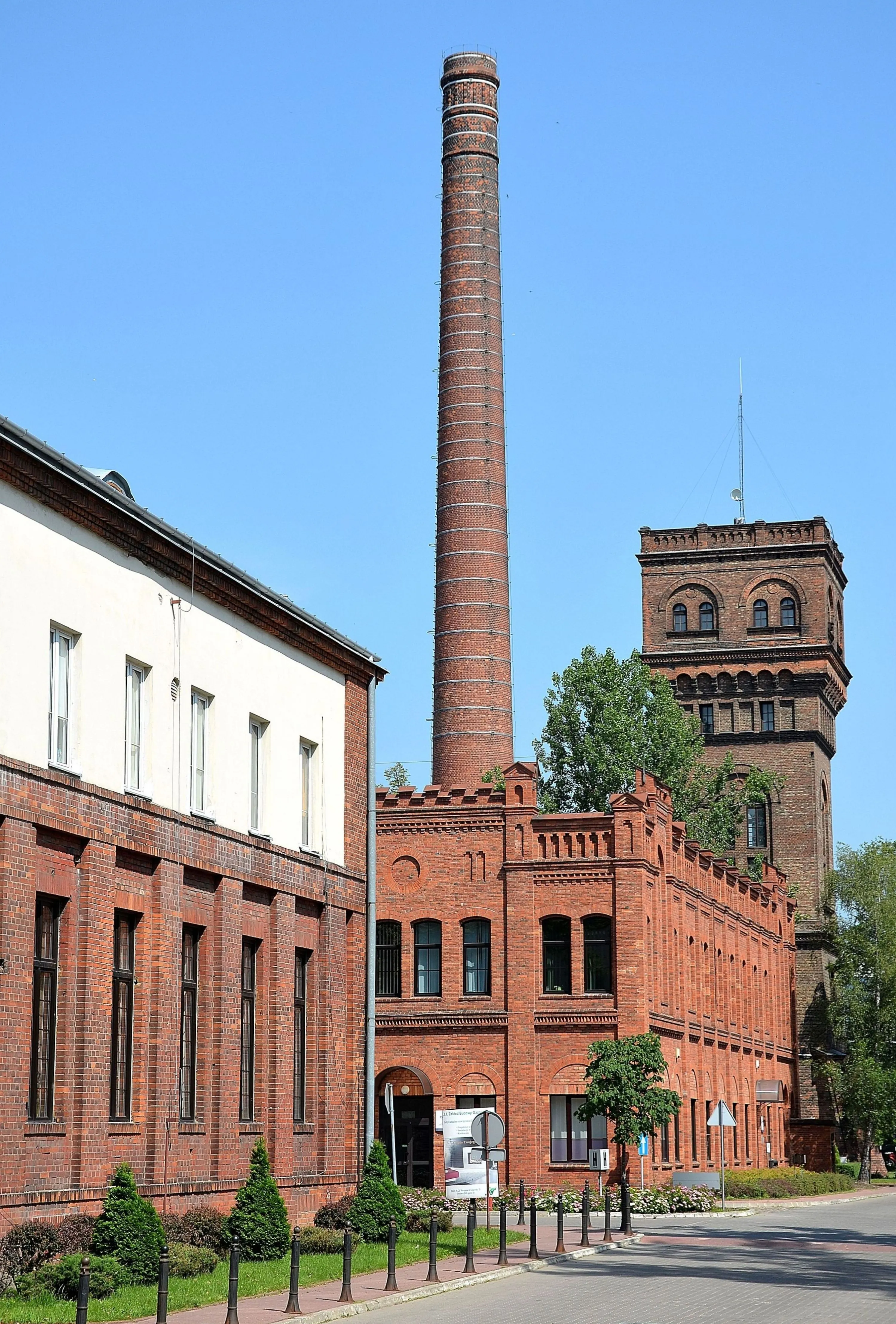 Red-brick industrial building with a tall chimney and a water tower under a clear blue sky