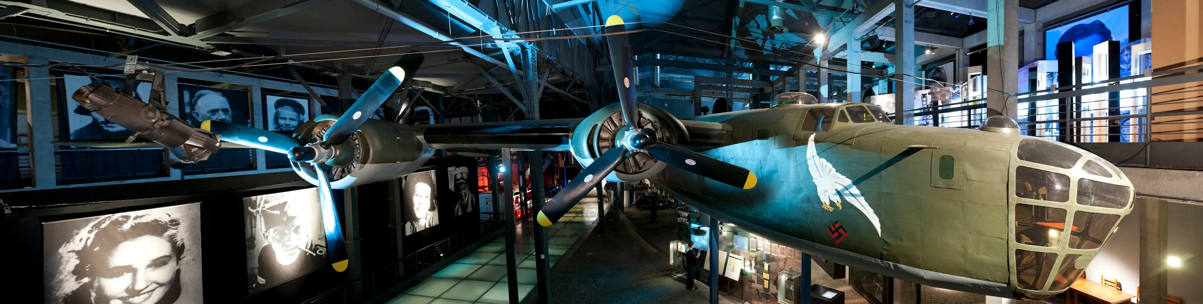 Un avión grande suspendido en un salón de museo con iluminación tenue y exhibiciones informativas en las paredes
